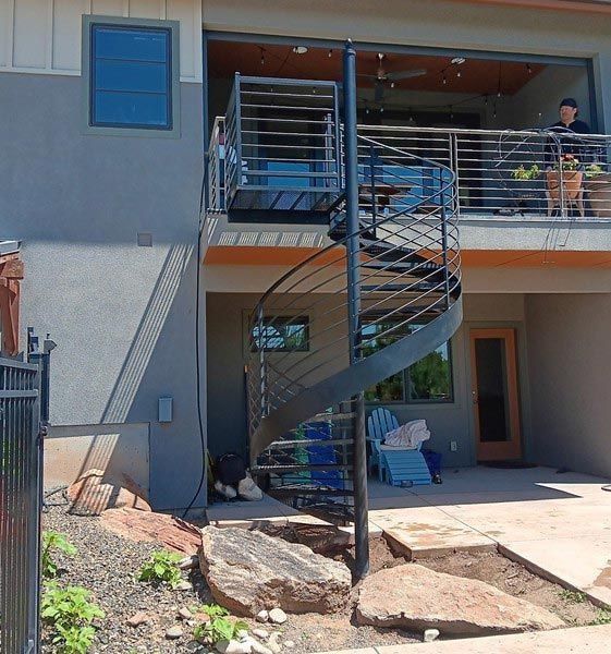 Black spiral staircase leading to an upper-level balcony on a two-story house.