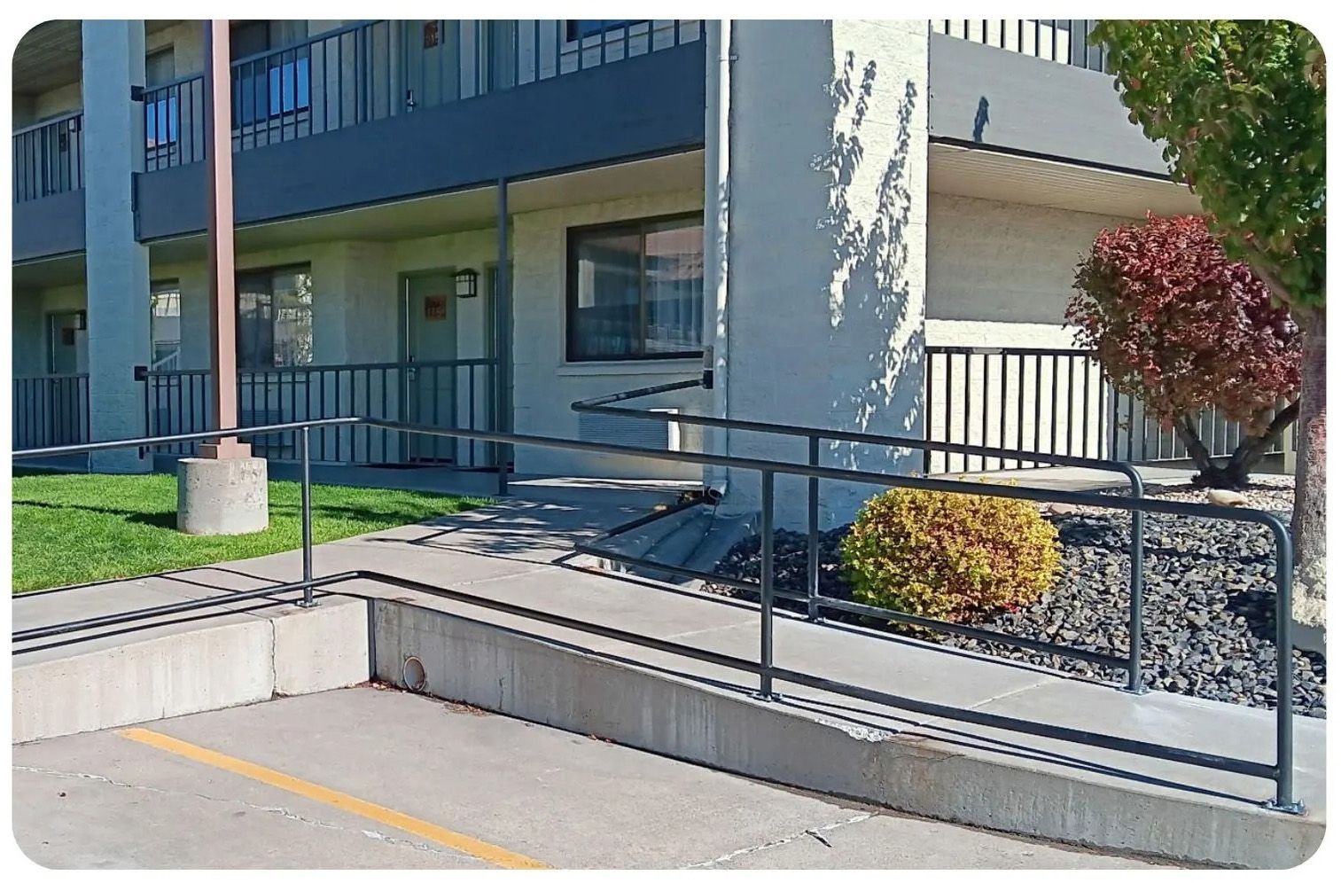 Exterior of building with ramp and railings for accessibility. Concrete barriers, green grass, and small bush.