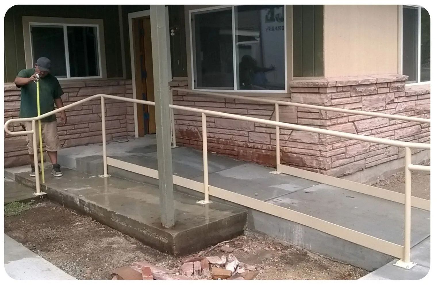 Person cleaning a concrete ramp with handrails leading to a building's entrance.