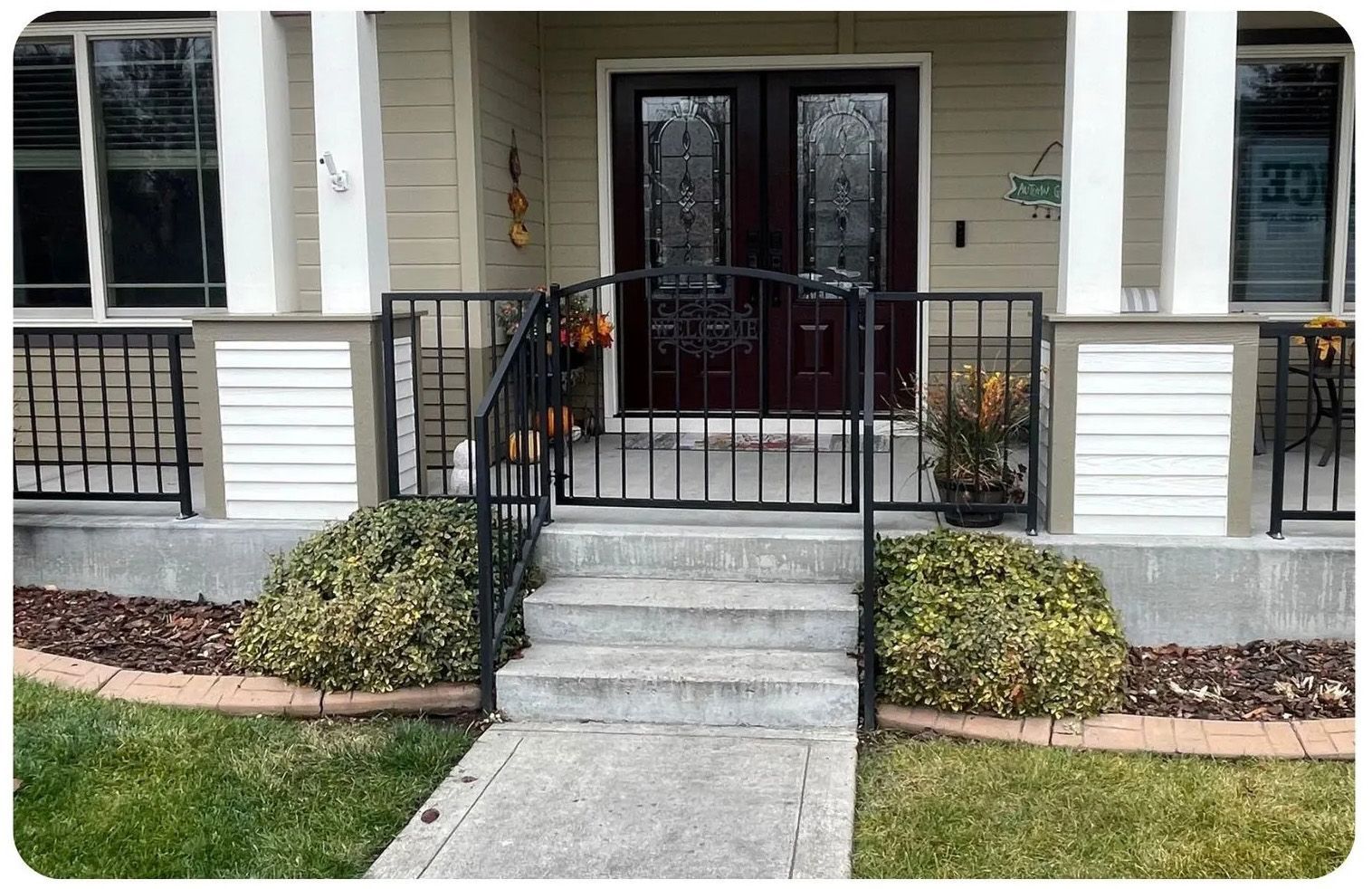 Front porch with concrete steps, wrought-iron railing, and dark double door entrance.