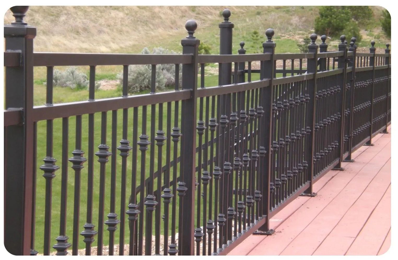 Black metal fence with decorative finials on a red deck overlooking a grassy area.