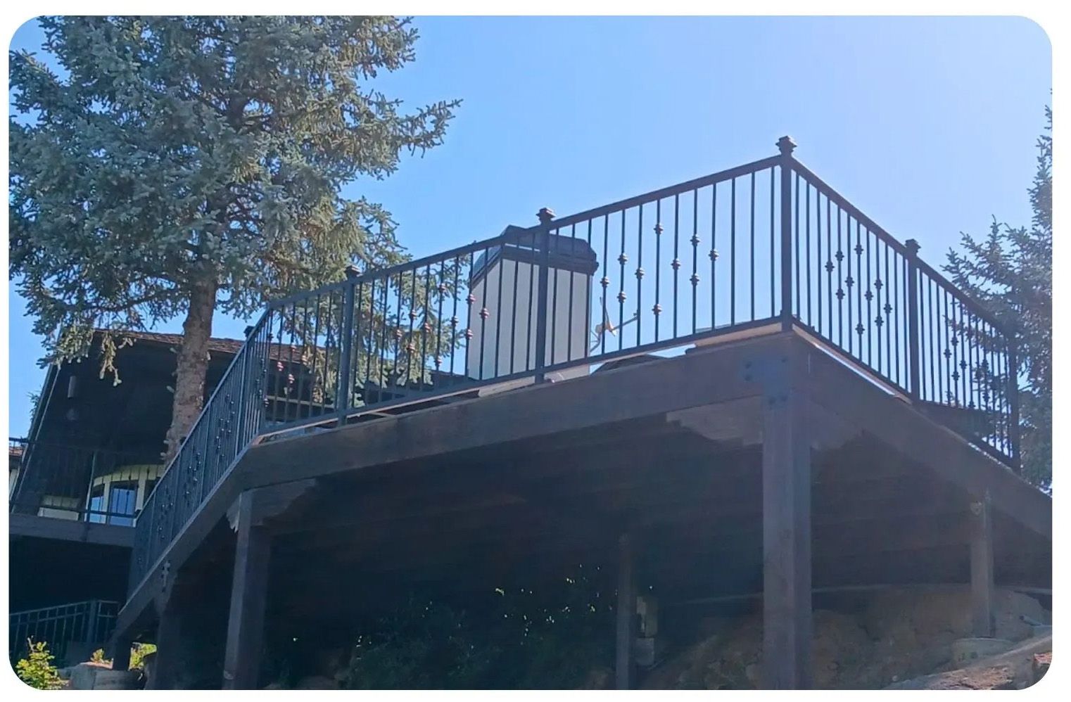 Wooden deck with black metal railing and a partial view of a building against a clear blue sky.