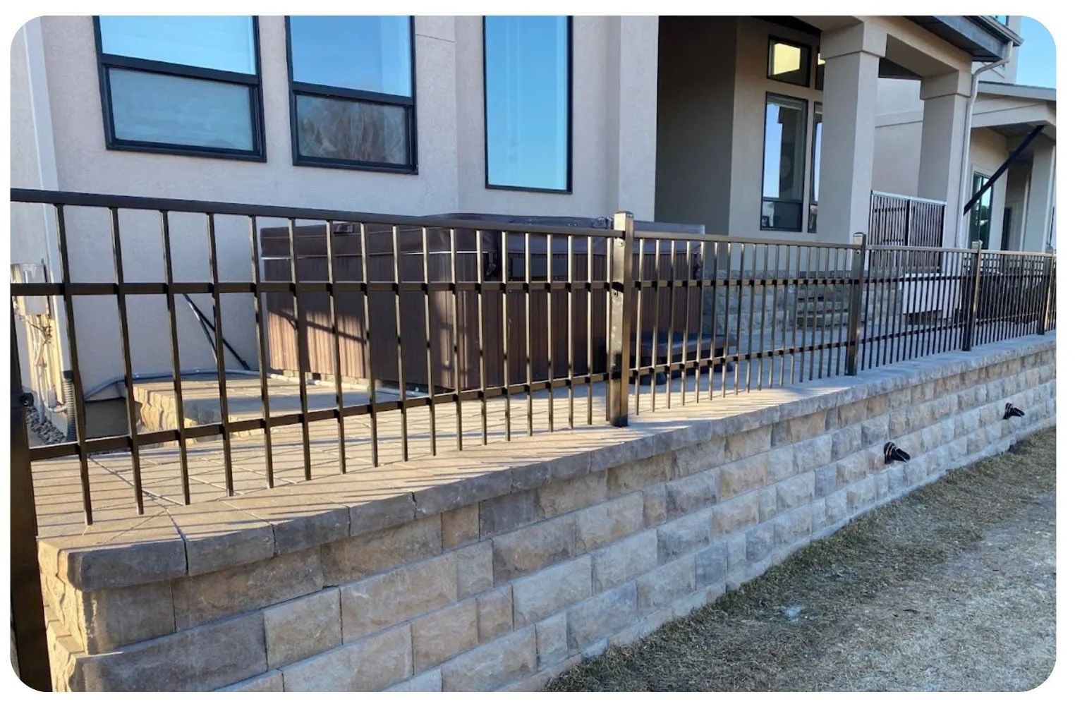 A brick retaining wall with black metal railing, hot tub, and house in background.
