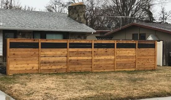 A modern horizontal wood fence with a black accent strip near the top, standing in a residential front yard.
