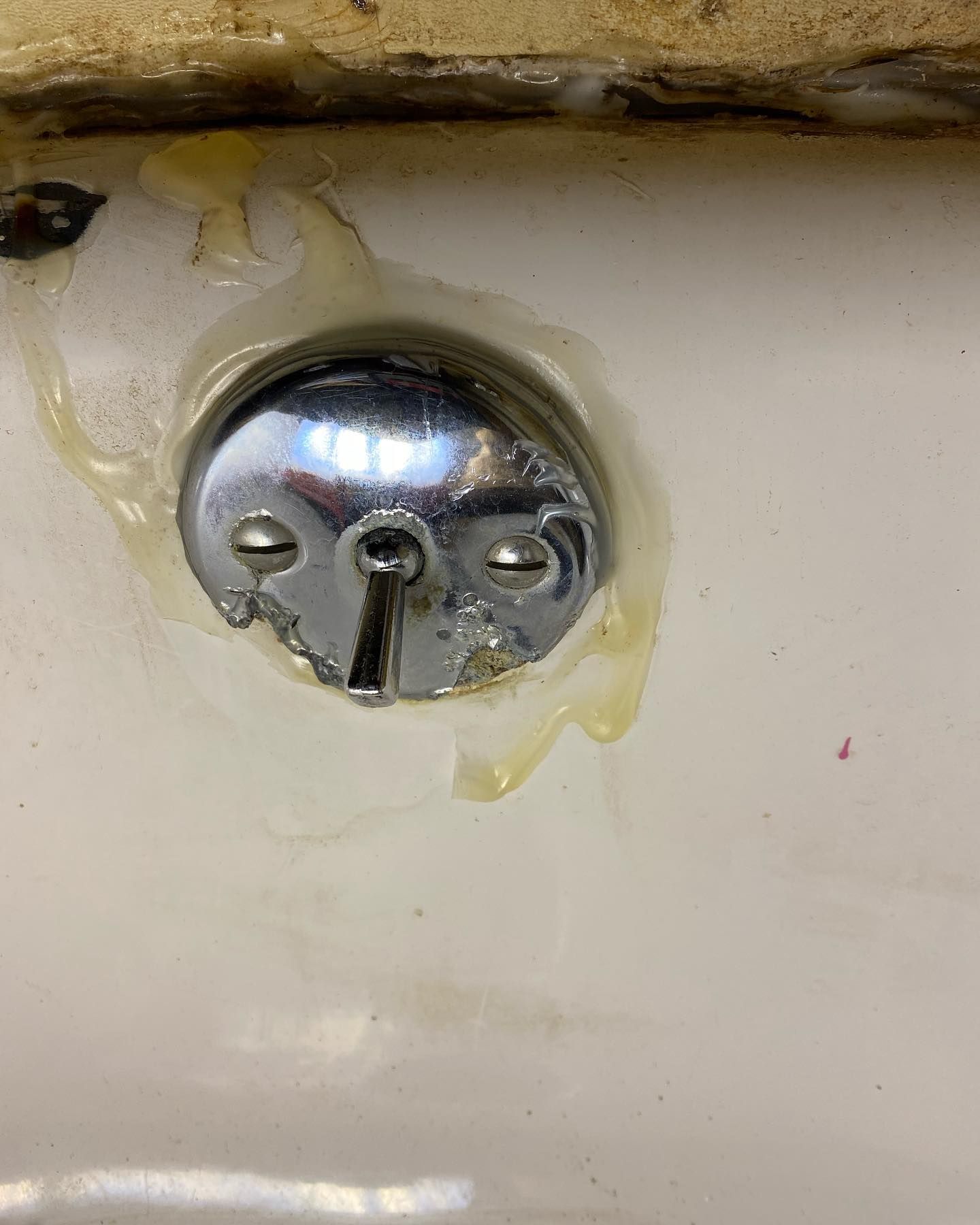 Chrome bathtub drain cover with yellow sealant and stains.