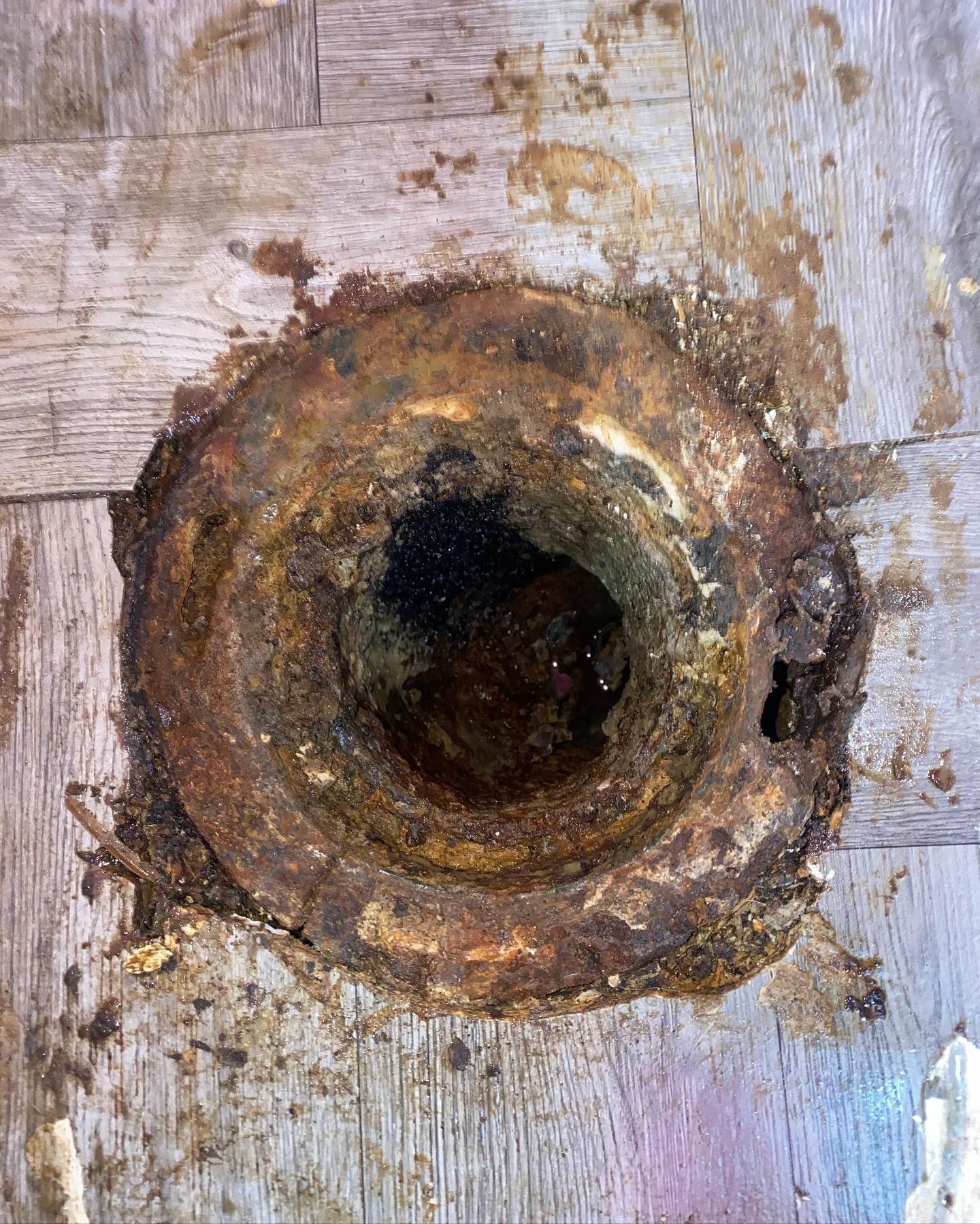 Corroded rusty metal toilet flange on damaged wooden floor, appearing in disrepair.
