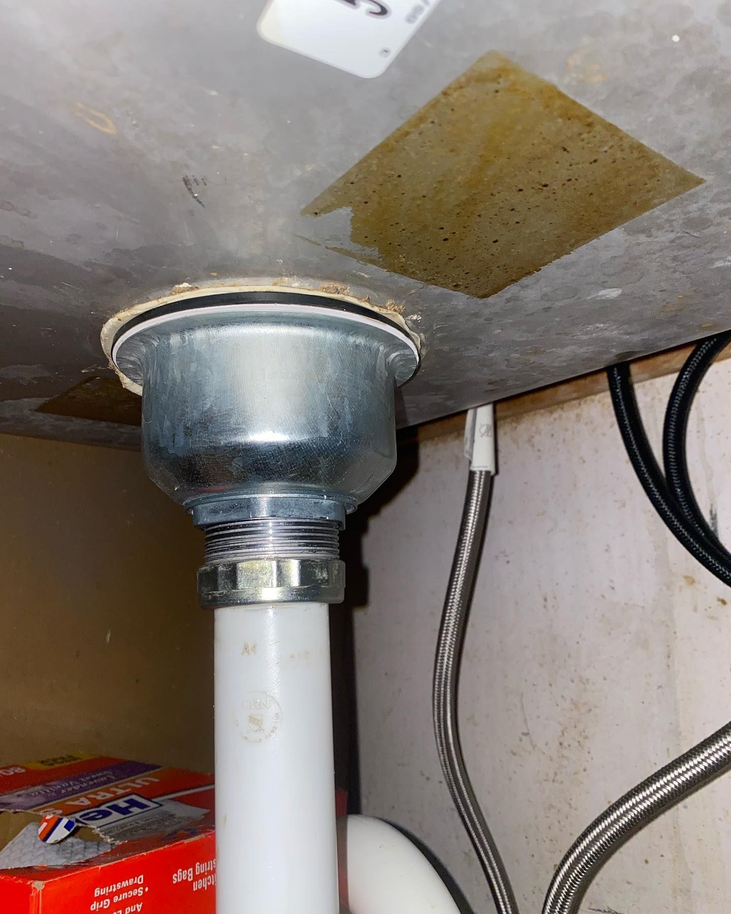 Underside of a kitchen sink, showing a drain basket connected to white and metallic plumbing.