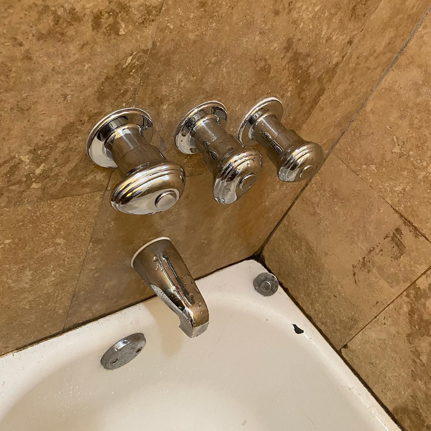 Chrome bathtub faucet and handles mounted on tan tile.