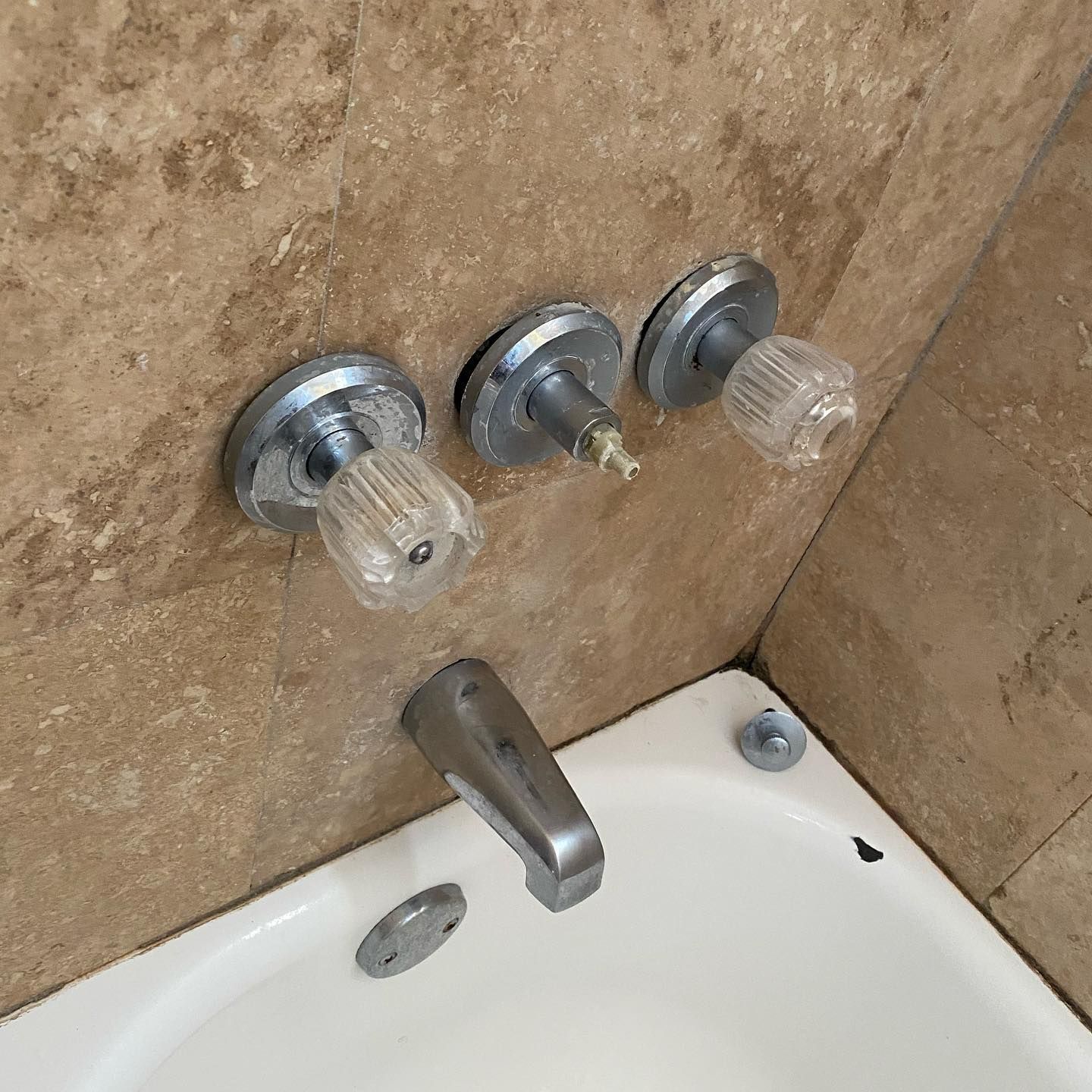Bathtub faucet with three knobs, one broken. Beige tile background.