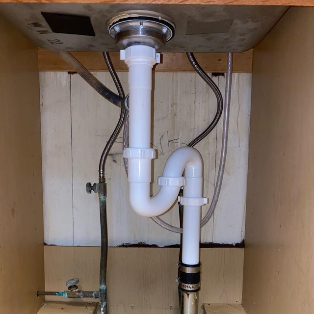 Under-sink plumbing: white P-trap connected to sink drain and drain pipe; copper supply lines and shutoff valve visible.