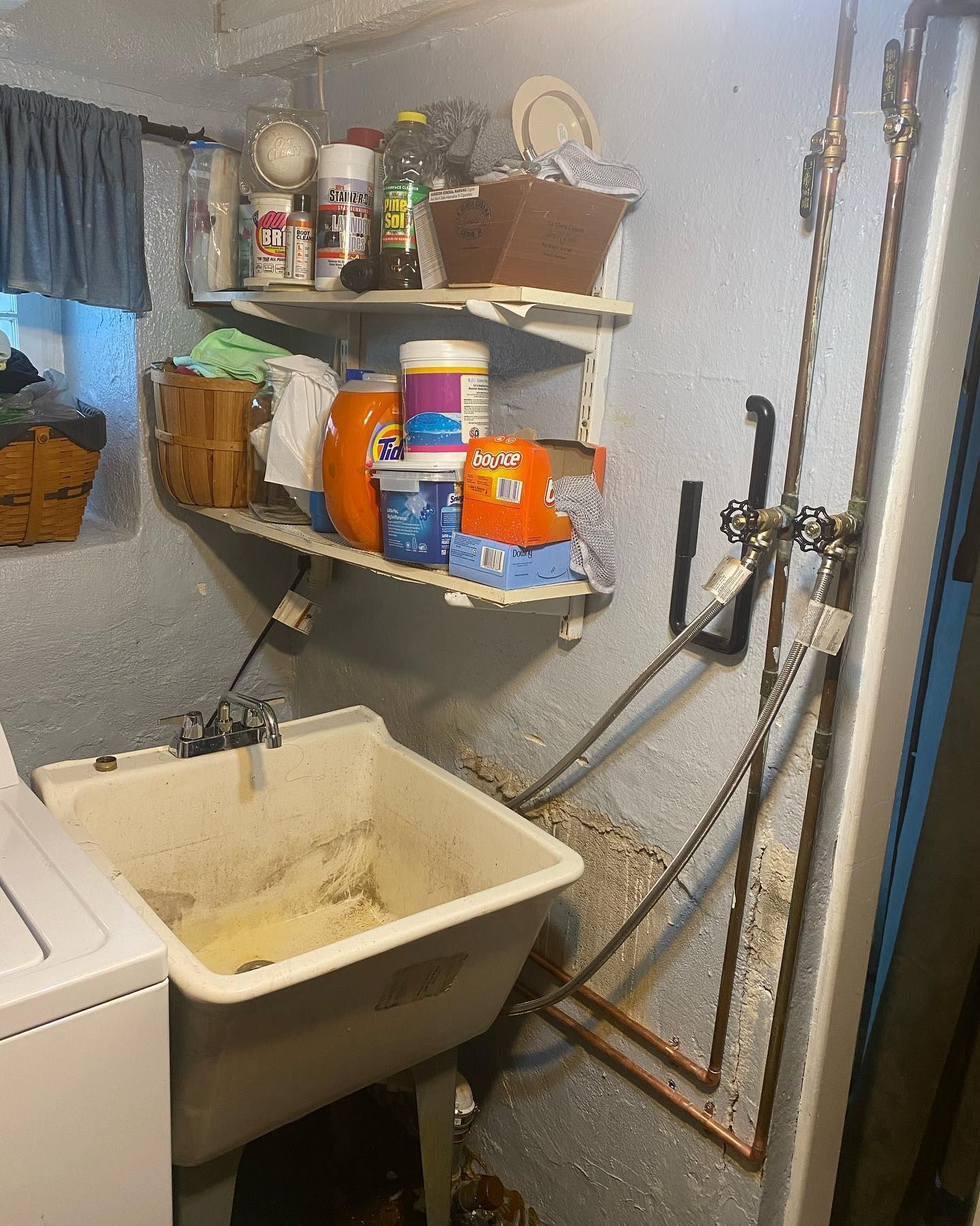 Laundry sink and supplies in a basement. Blue wall, white shelves with detergent and cleaning products.