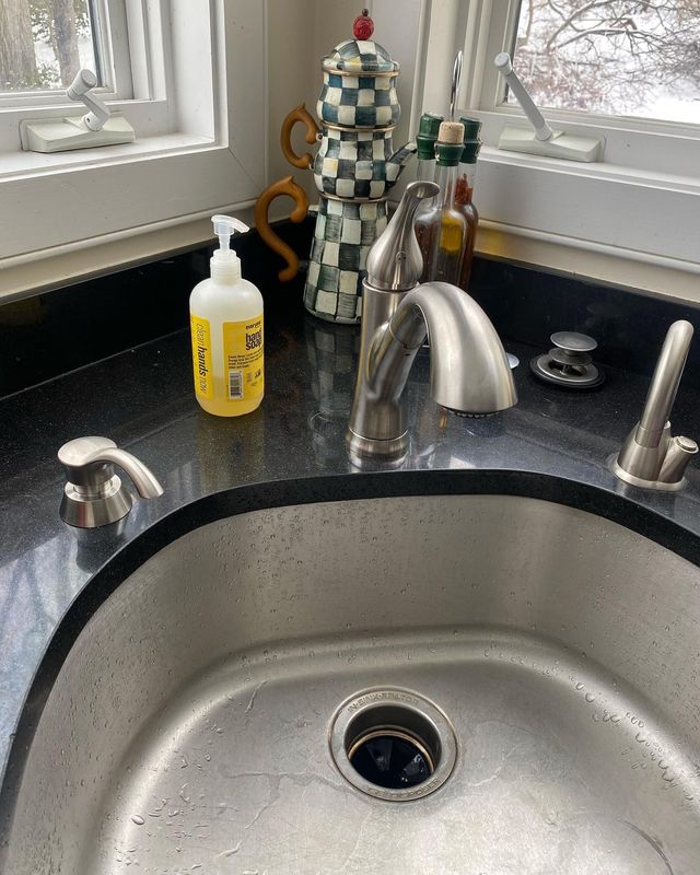 Kitchen sink with black granite countertop, chrome faucet, and soap dispenser.