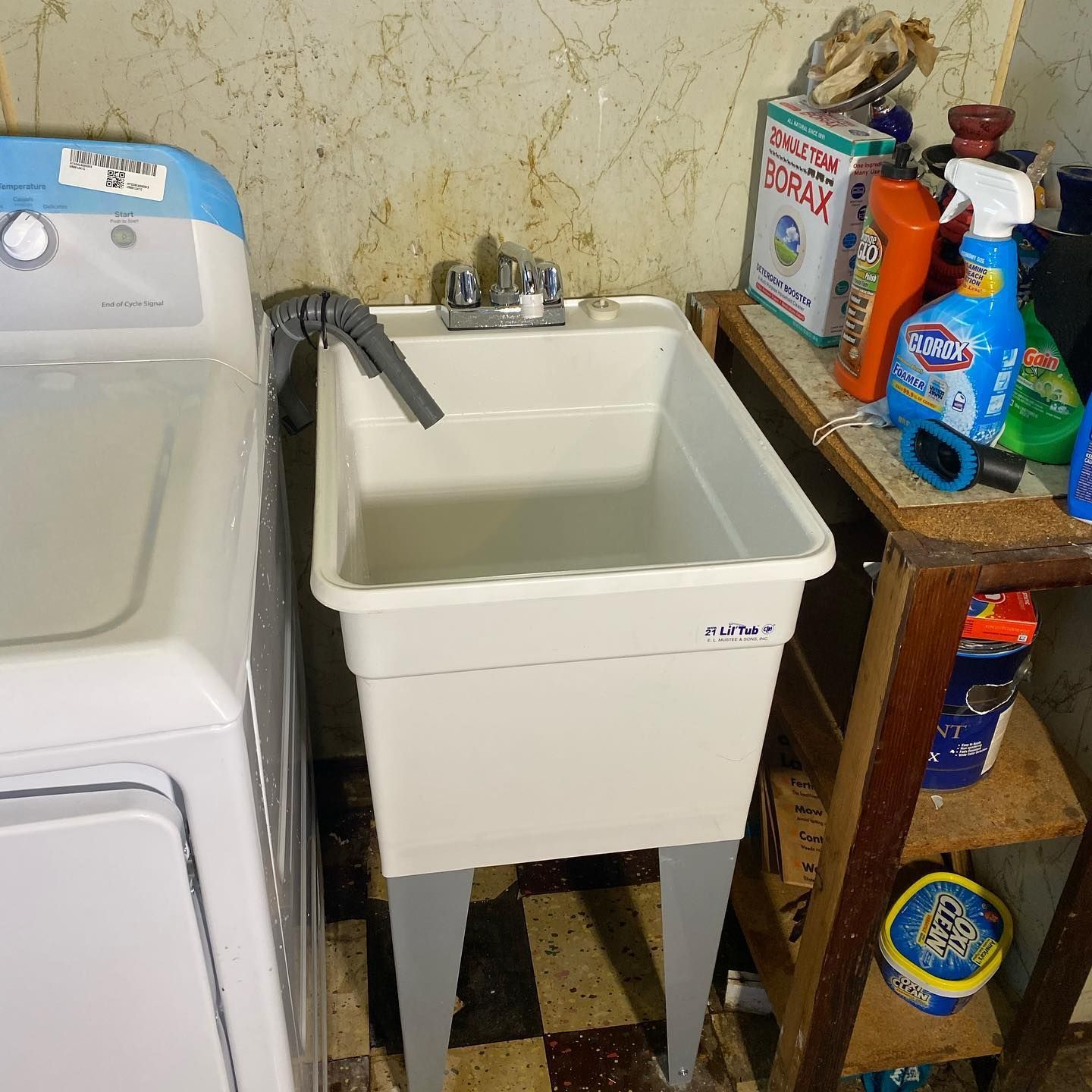 Laundry room with a white utility sink, washing machine, and cleaning supplies on a small shelf.