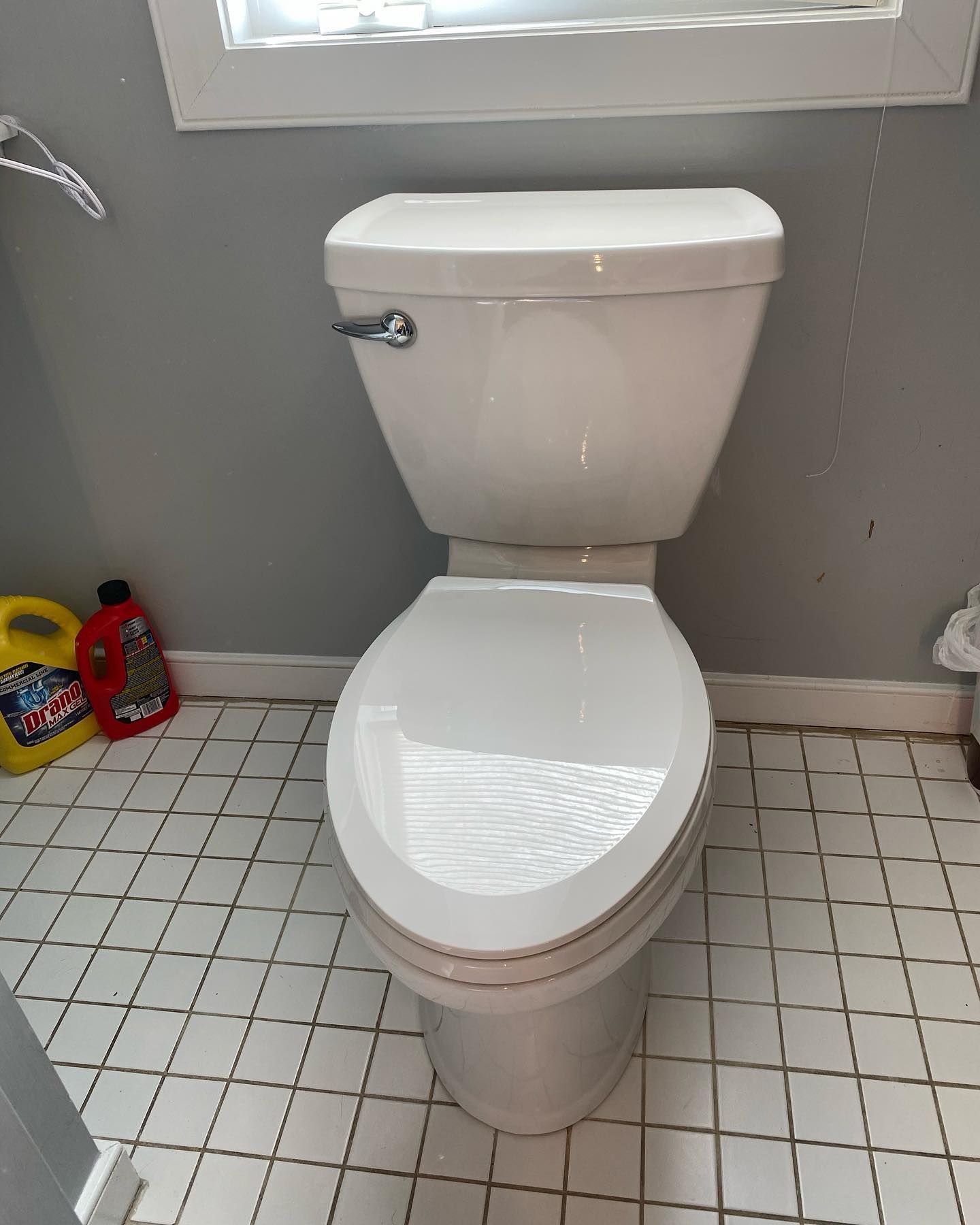 White toilet in a bathroom, white tile floor, gray walls.