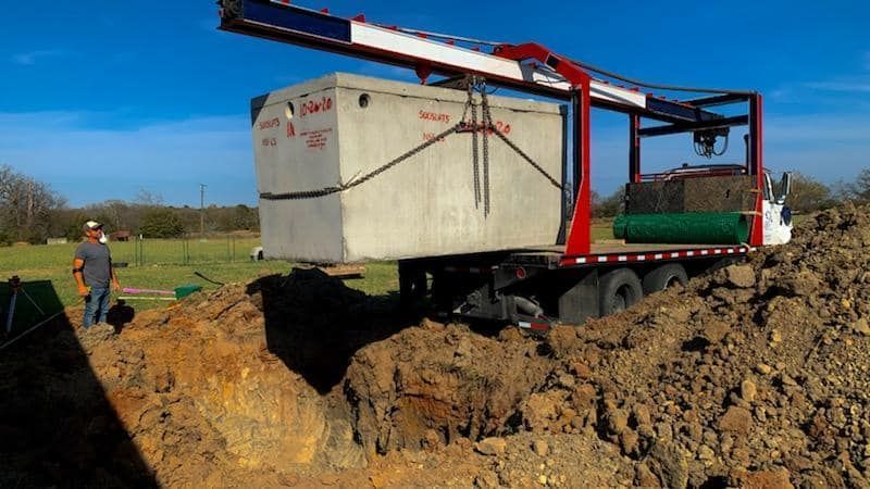 a man is standing in the dirt next to a truck carrying a septic tank .