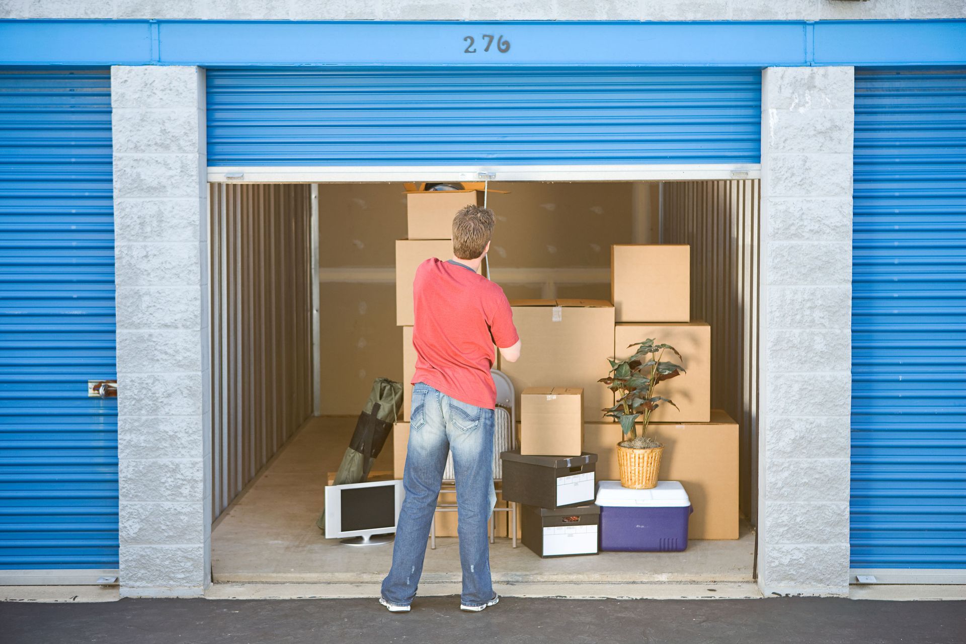 A man in a red shirt is standing in a storage unit filled with boxes