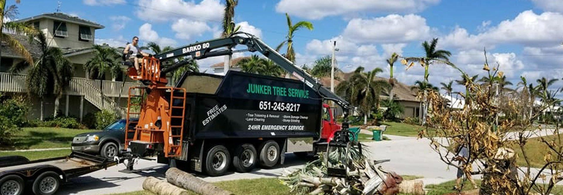 Black truck and orange crane clearing storm debris beside damaged palm trees in a tropical neighborhood