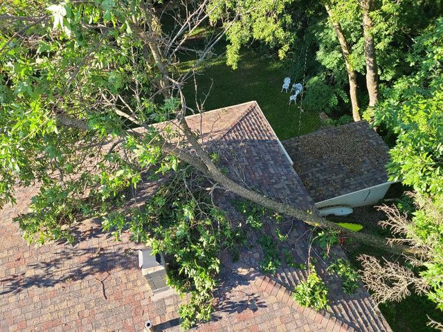 Aerial view of a house roof surrounded by green trees and yard.