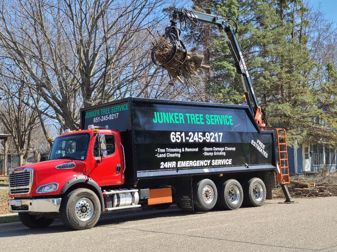 Red and black Junker Tree Service truck parked outdoors with a ladder on the side.