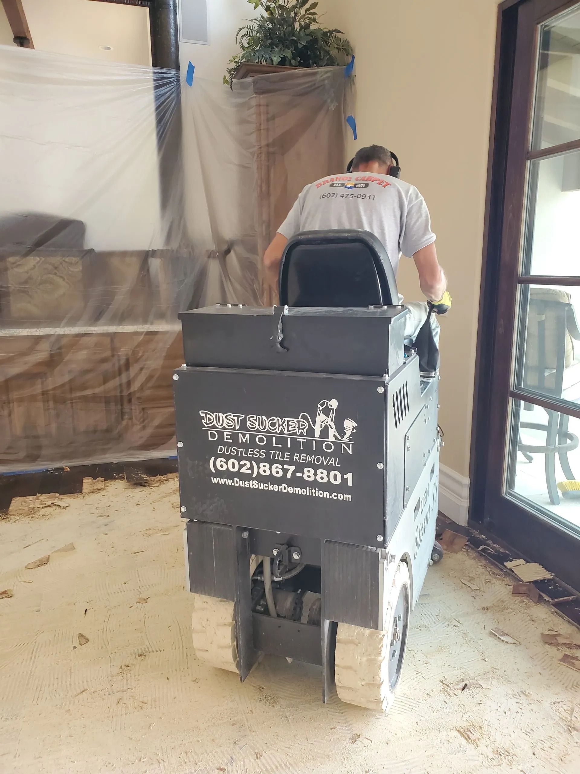 A man is using a machine to remove carpet in a living room.