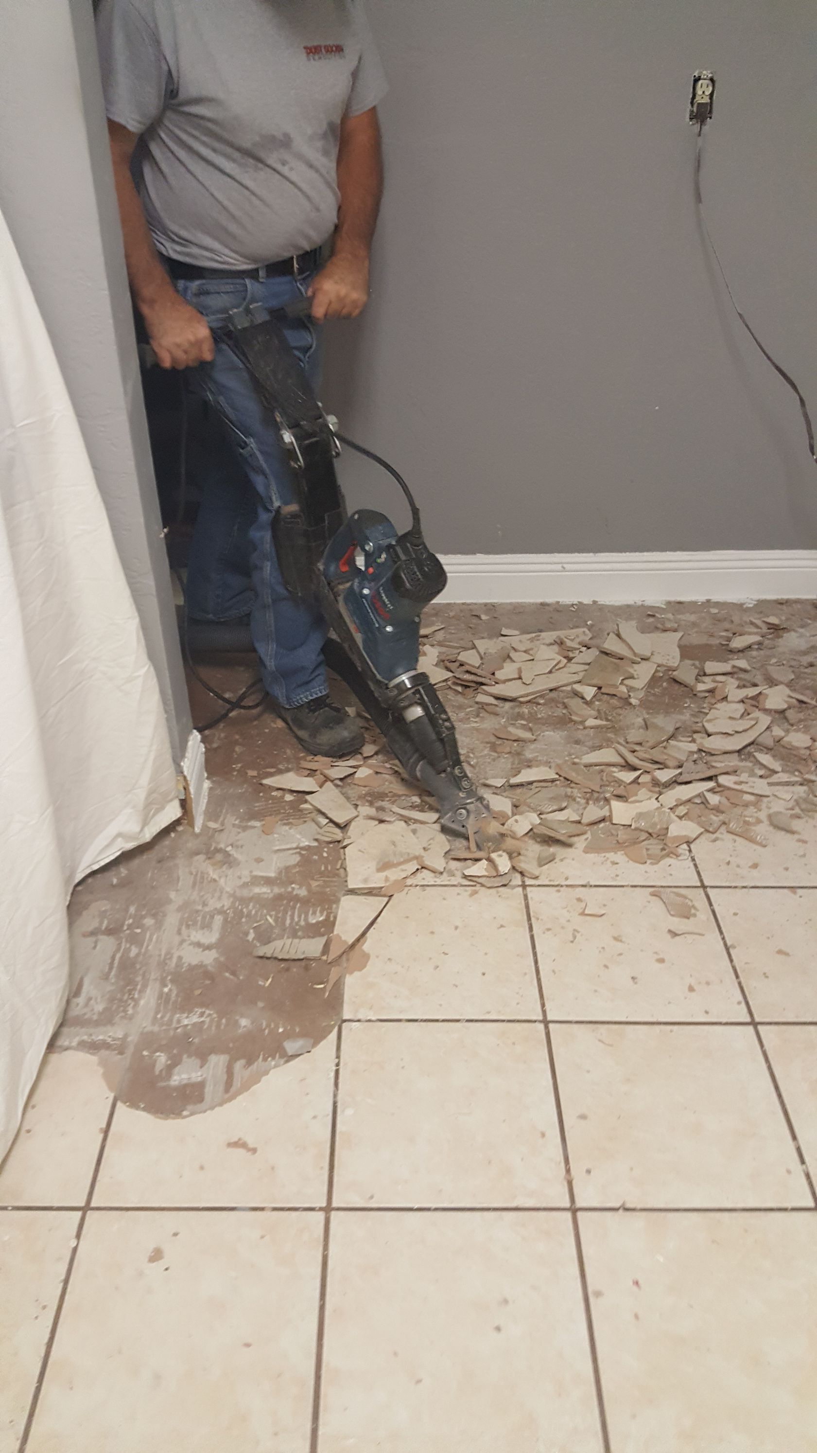 A man is using a hammer to remove tile from the floor.