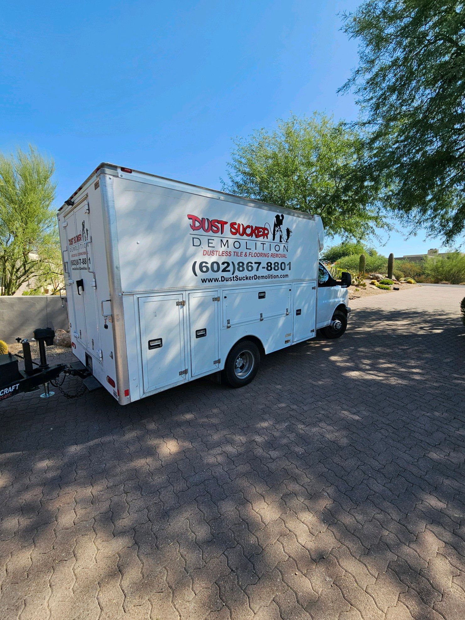 A white van with a trailer attached to it is parked in a parking lot.