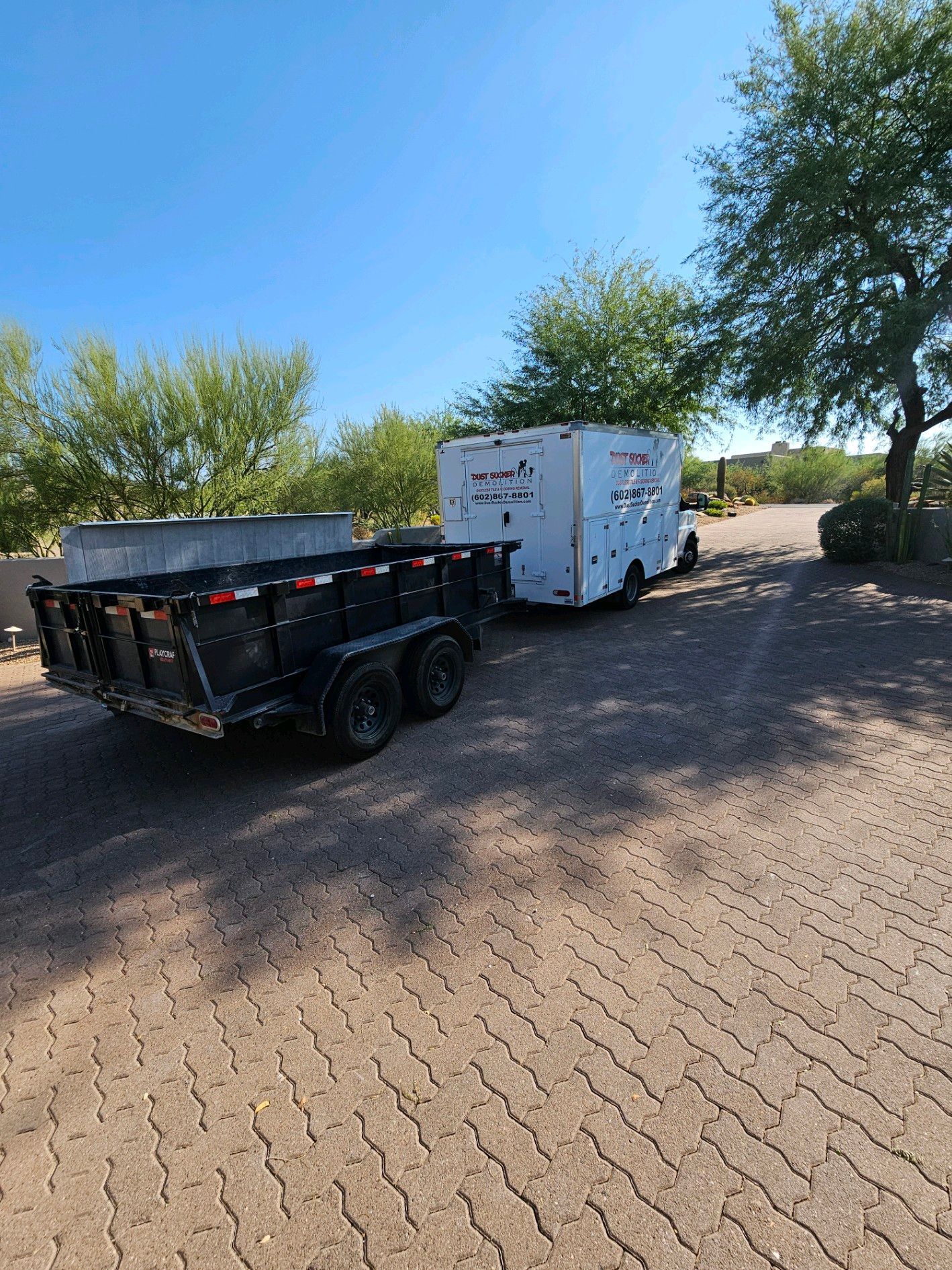 A dump truck with a trailer attached to it is parked on a brick road.