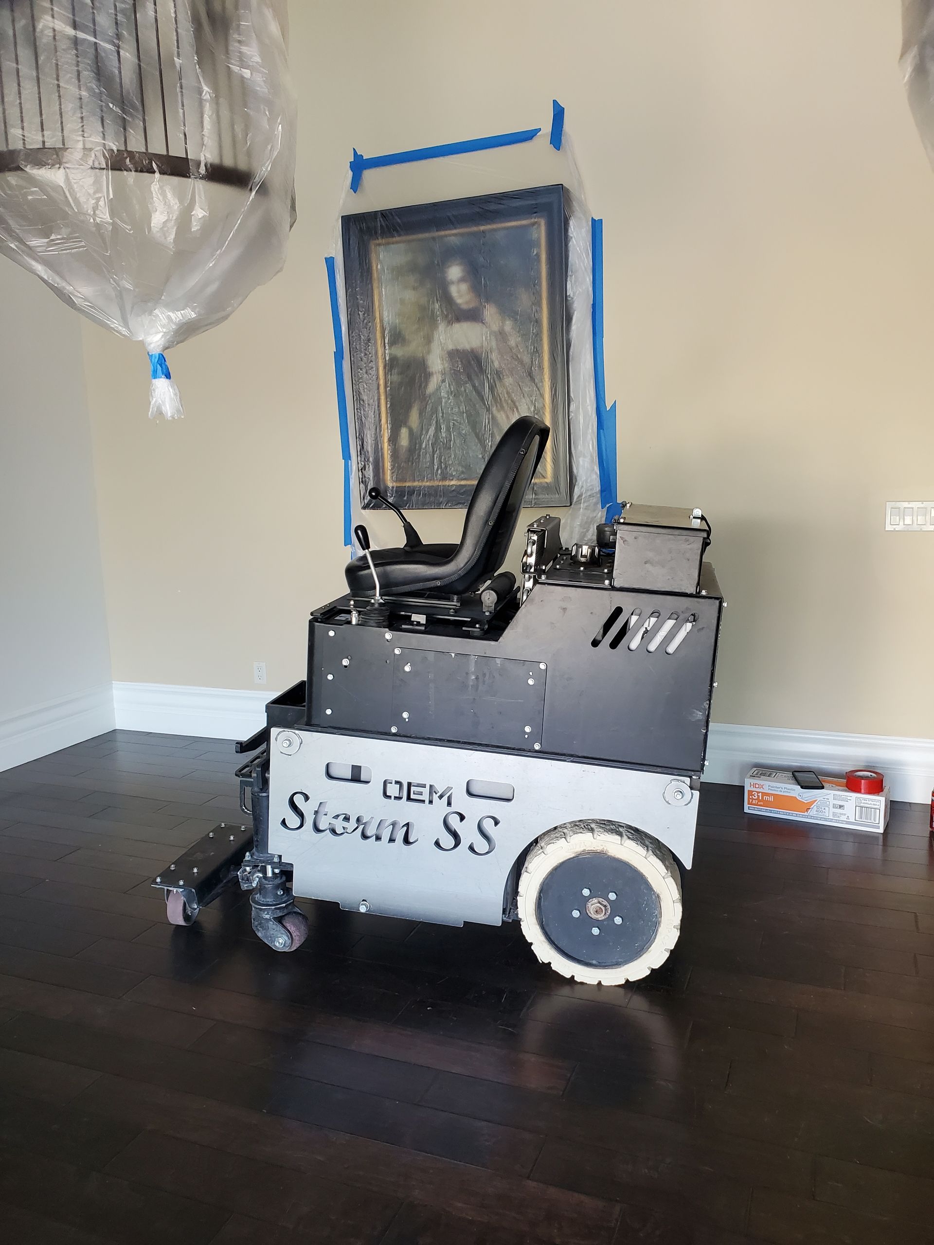 A machine is sitting on a wooden floor in a room with a picture on the wall.