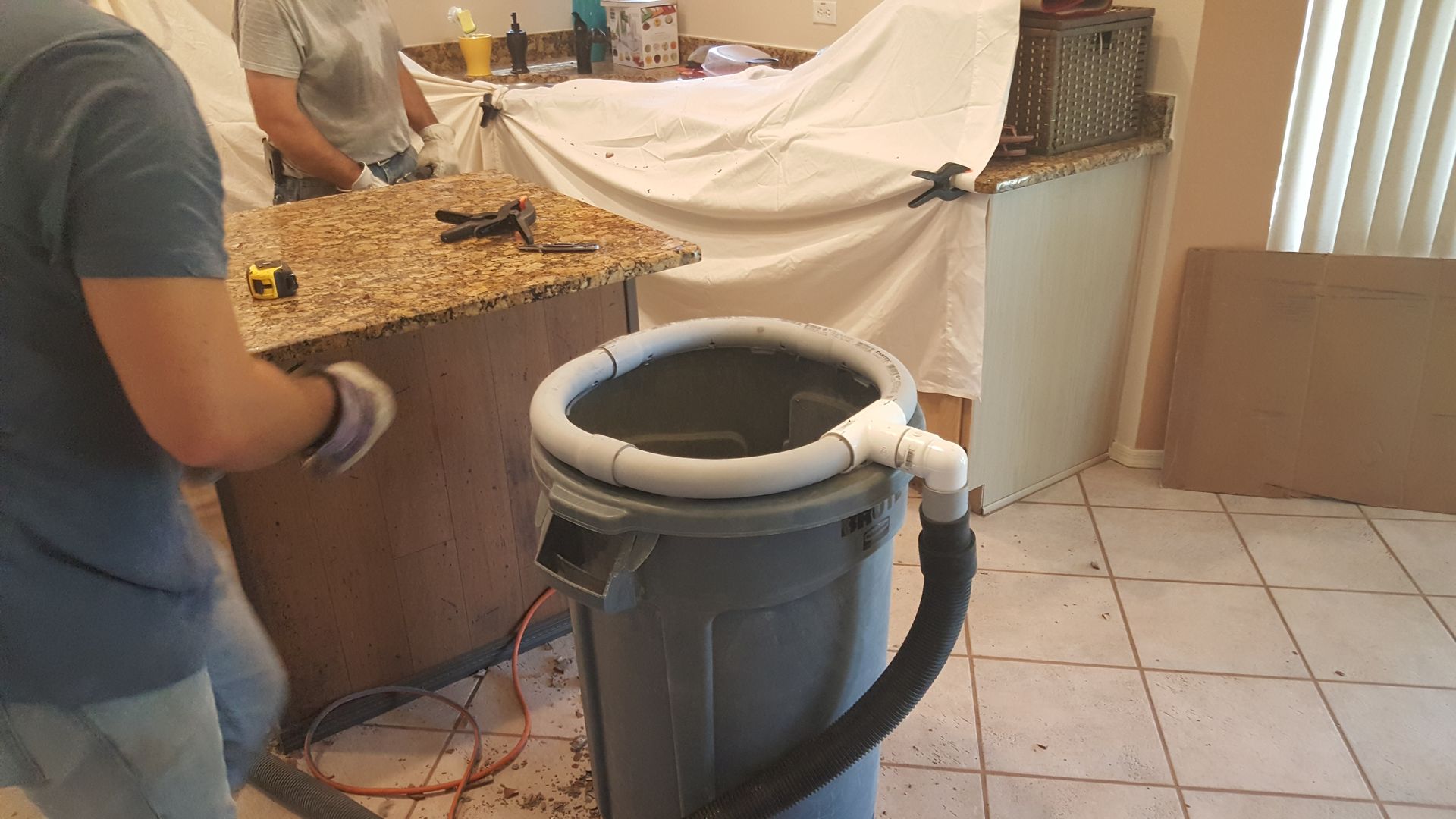A man is standing next to a trash can in a kitchen.