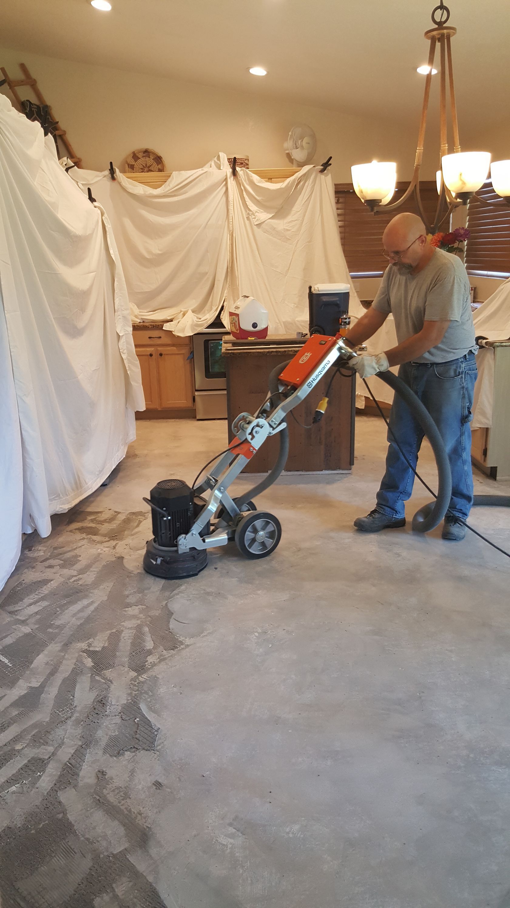 A man is using a grinder on a concrete floor in a kitchen.