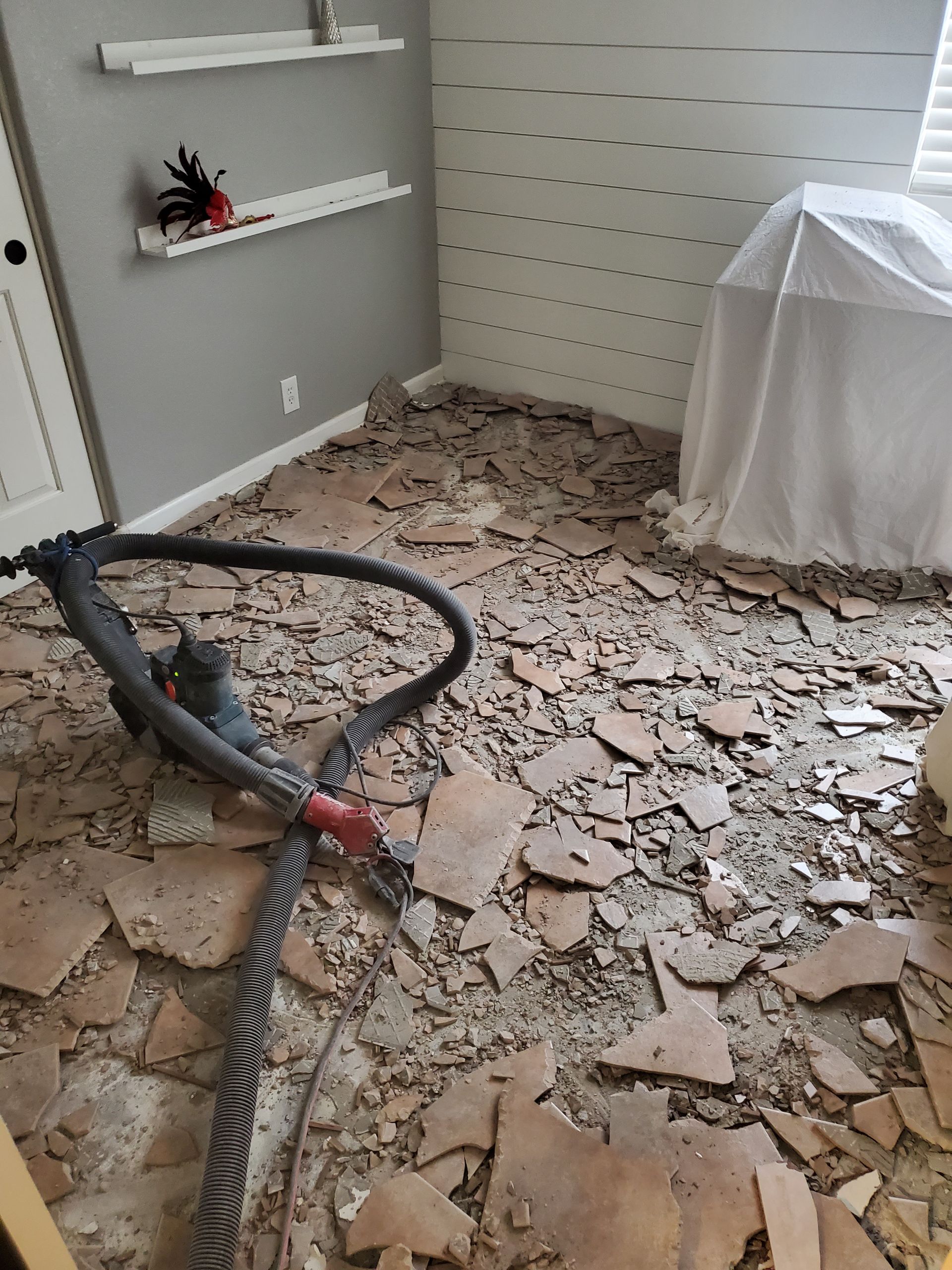 A vacuum cleaner is sitting on a pile of broken tiles in a room.