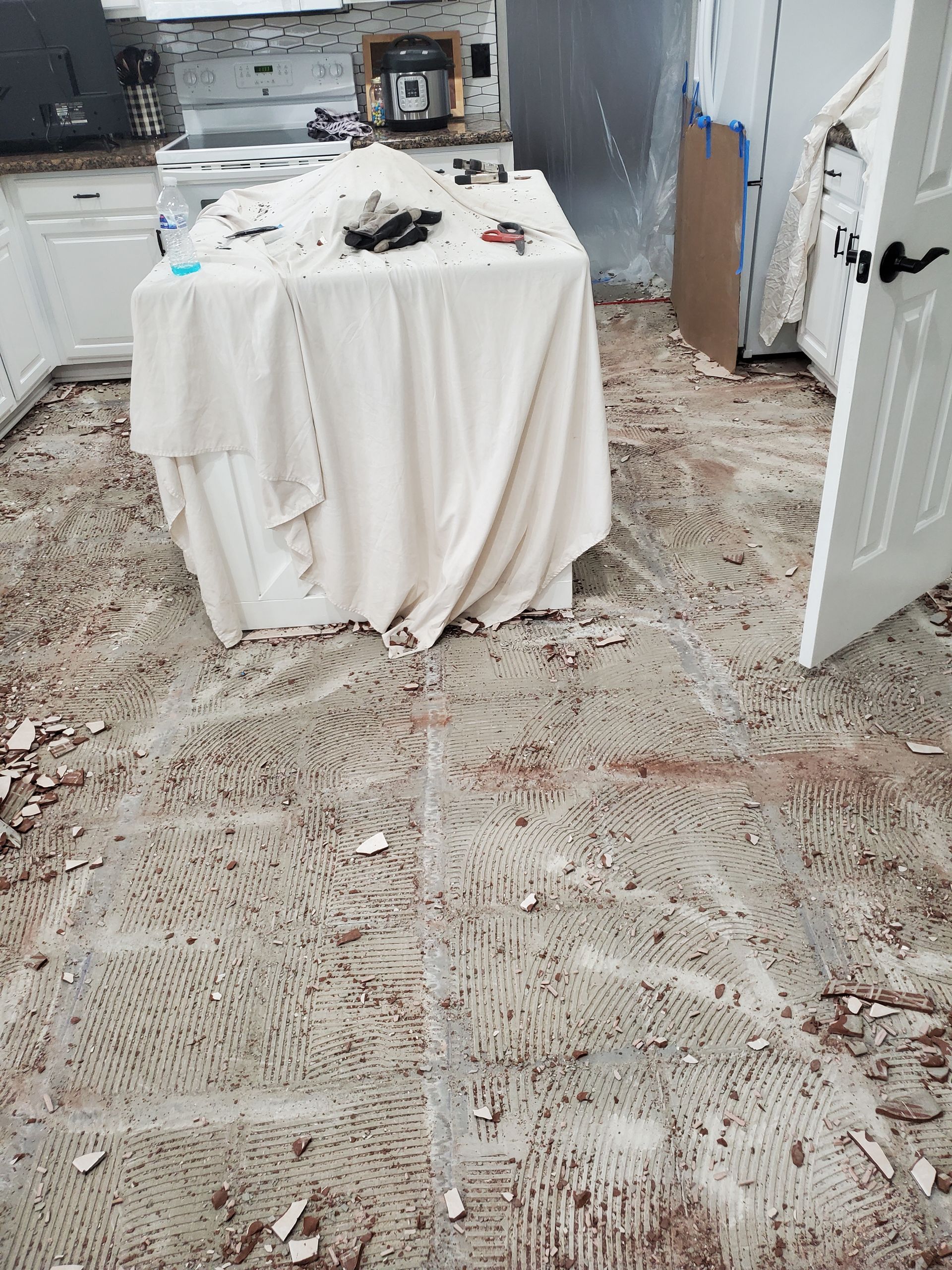 A kitchen with a dirty floor and a table with a white cloth on it.