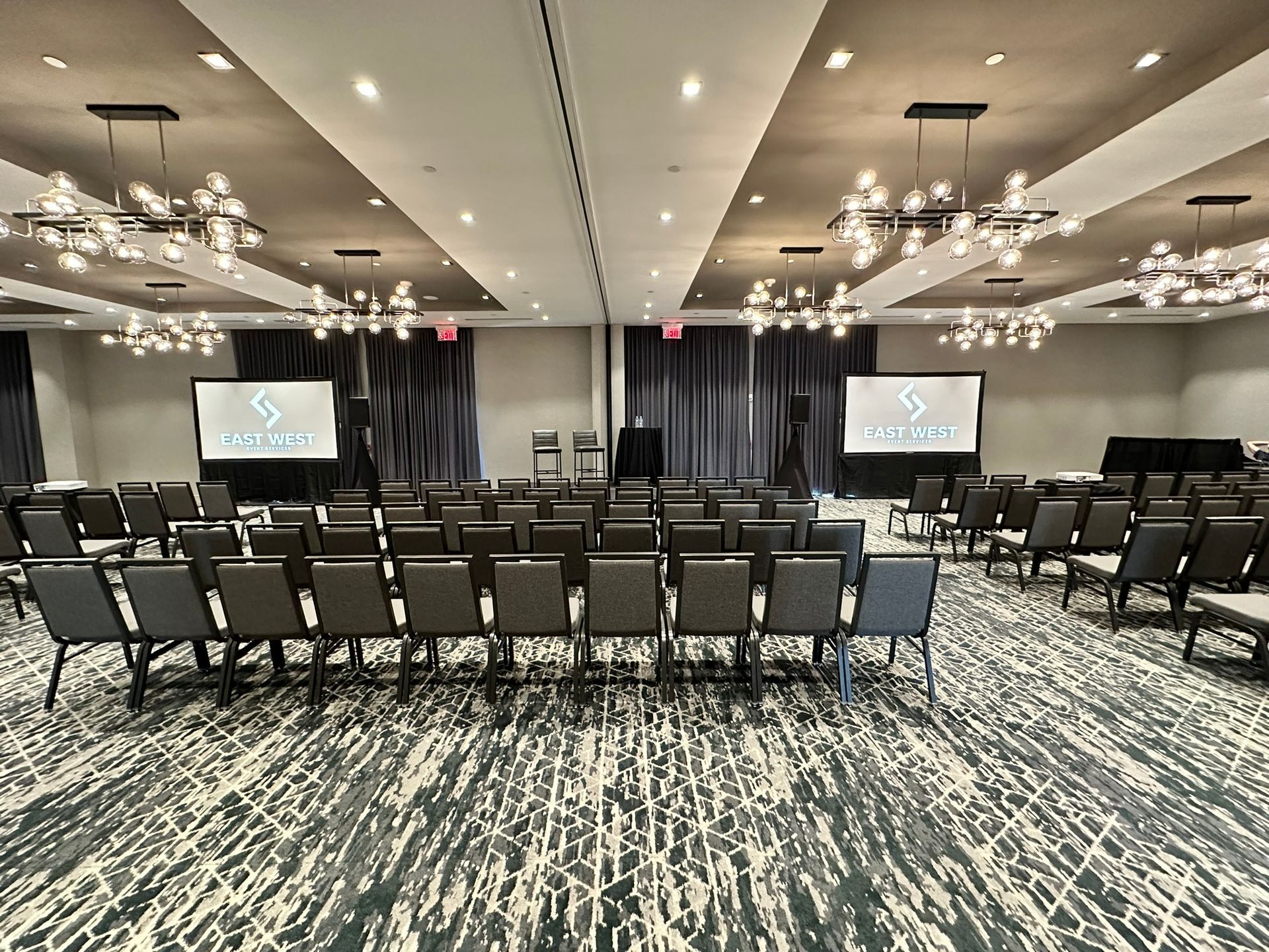 Conference room set up for a presentation; rows of chairs facing two screens with logos.