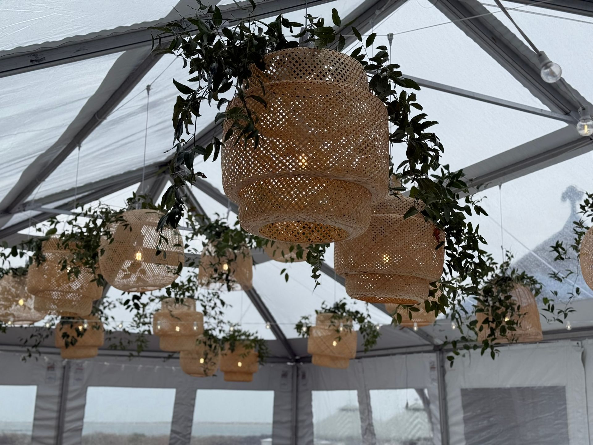 Woven pendant lights with greenery, hanging inside a clear tent.