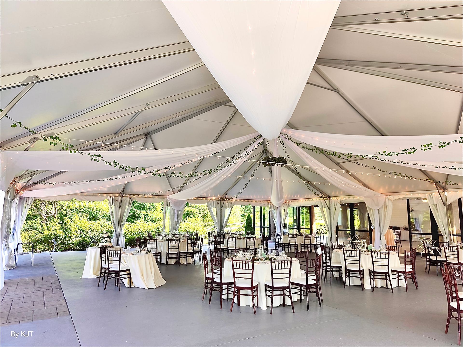 Wedding reception tent with round tables, chairs, and draped ceiling.