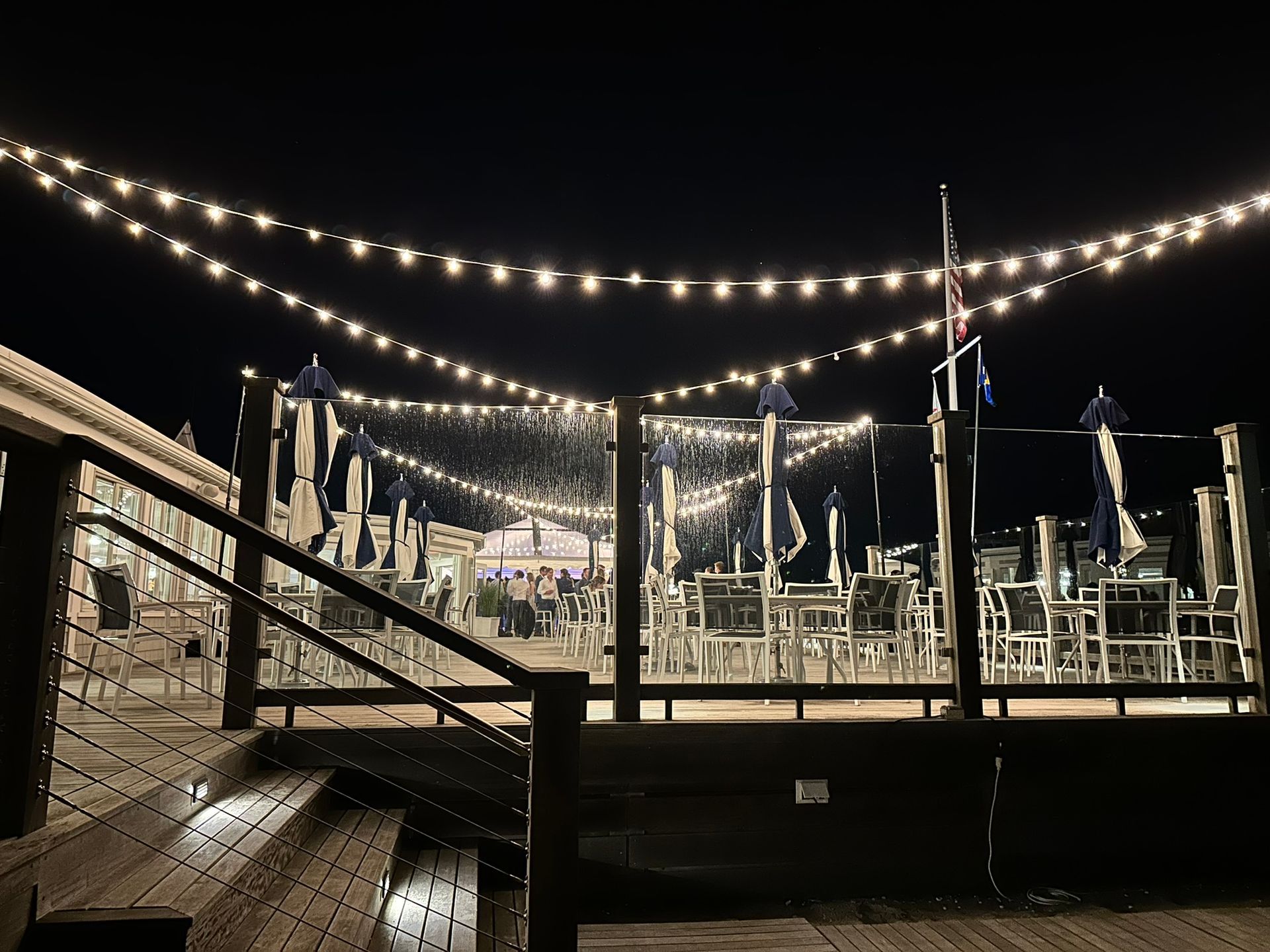 Nighttime outdoor dining area with string lights, tables, and umbrellas.