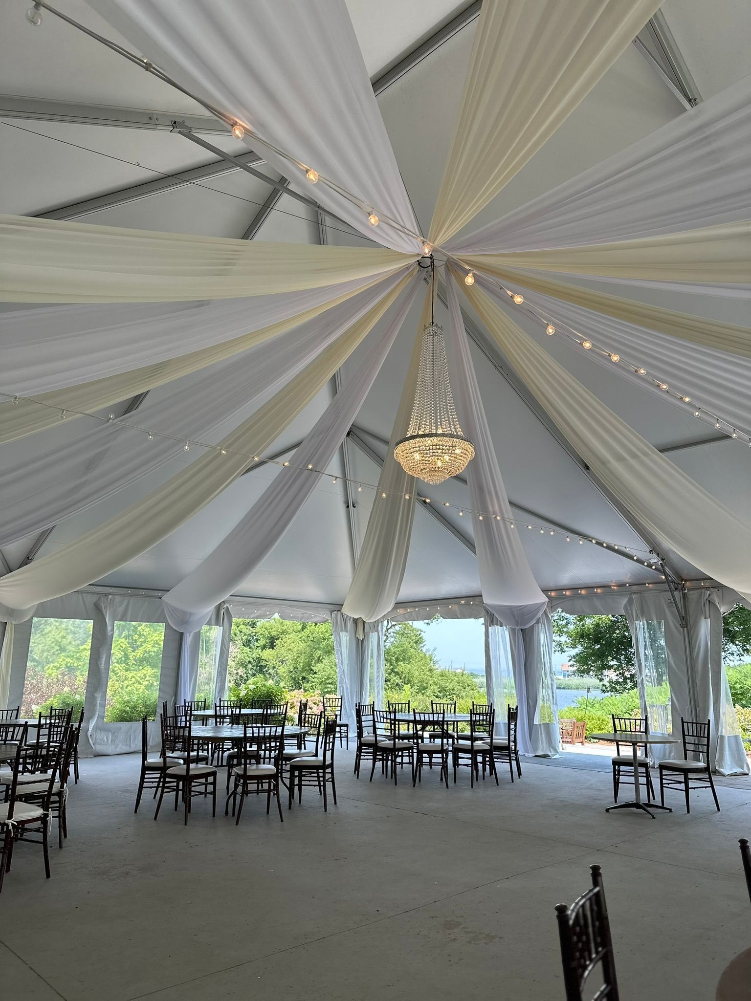 Tent interior with draped fabric, chandelier, tables, and chairs.