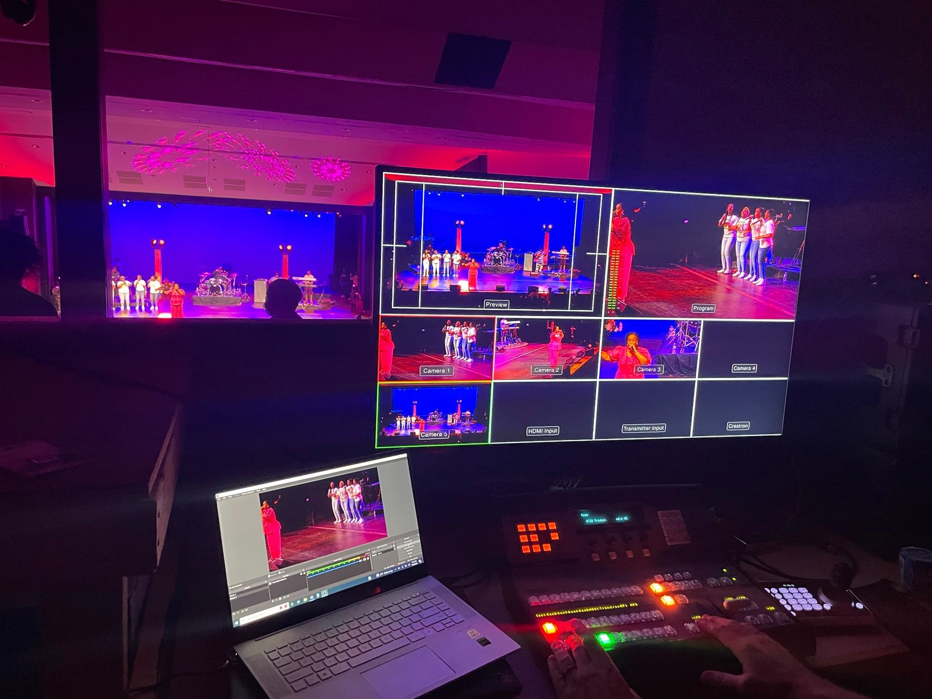 A person operates a live video production setup with monitors displaying a stage performance.