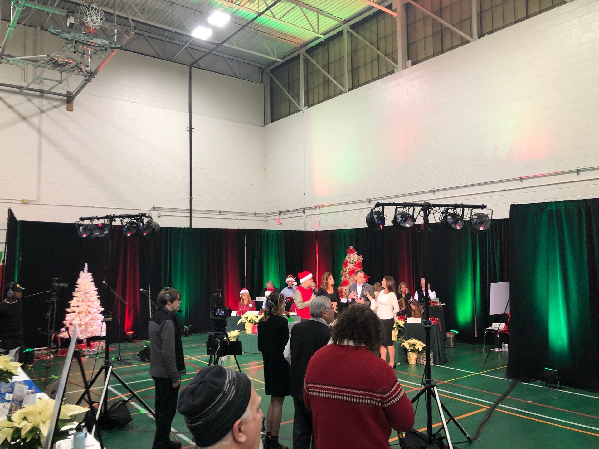People gathered on a stage with red and green decor, lights, and a Christmas tree, in a large venue.