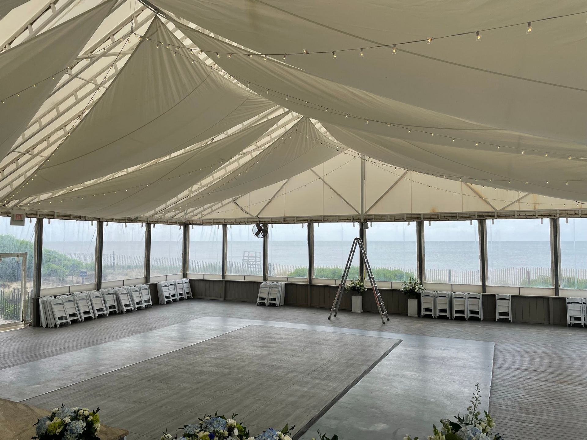 Inside a wedding tent overlooking the ocean, with chairs and a dance floor.