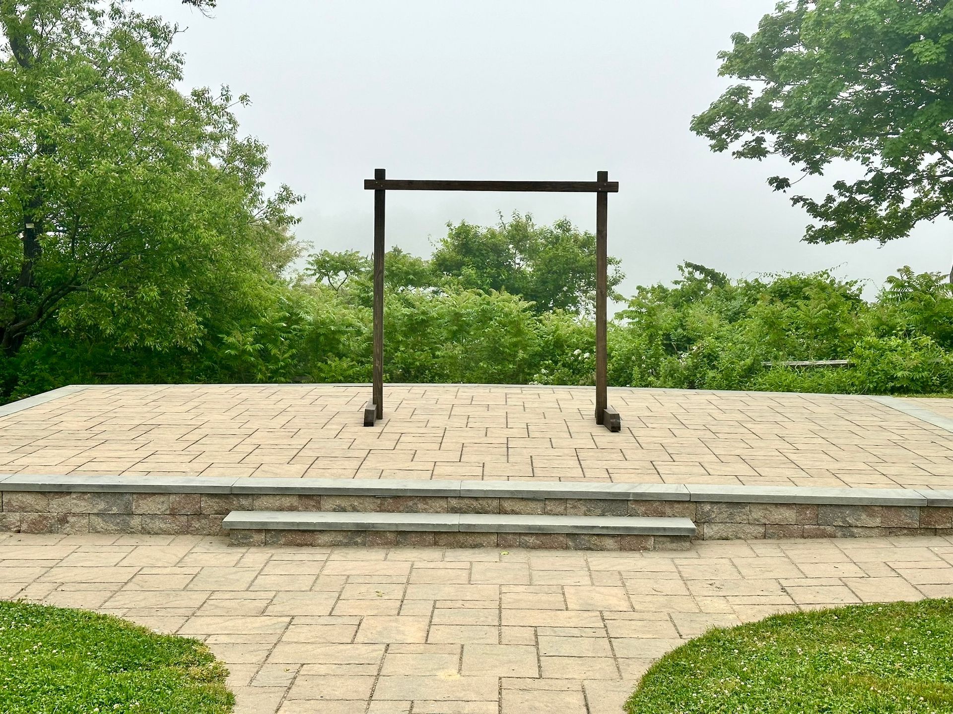 Wooden wedding arch on a stone patio, overlooking a foggy landscape.