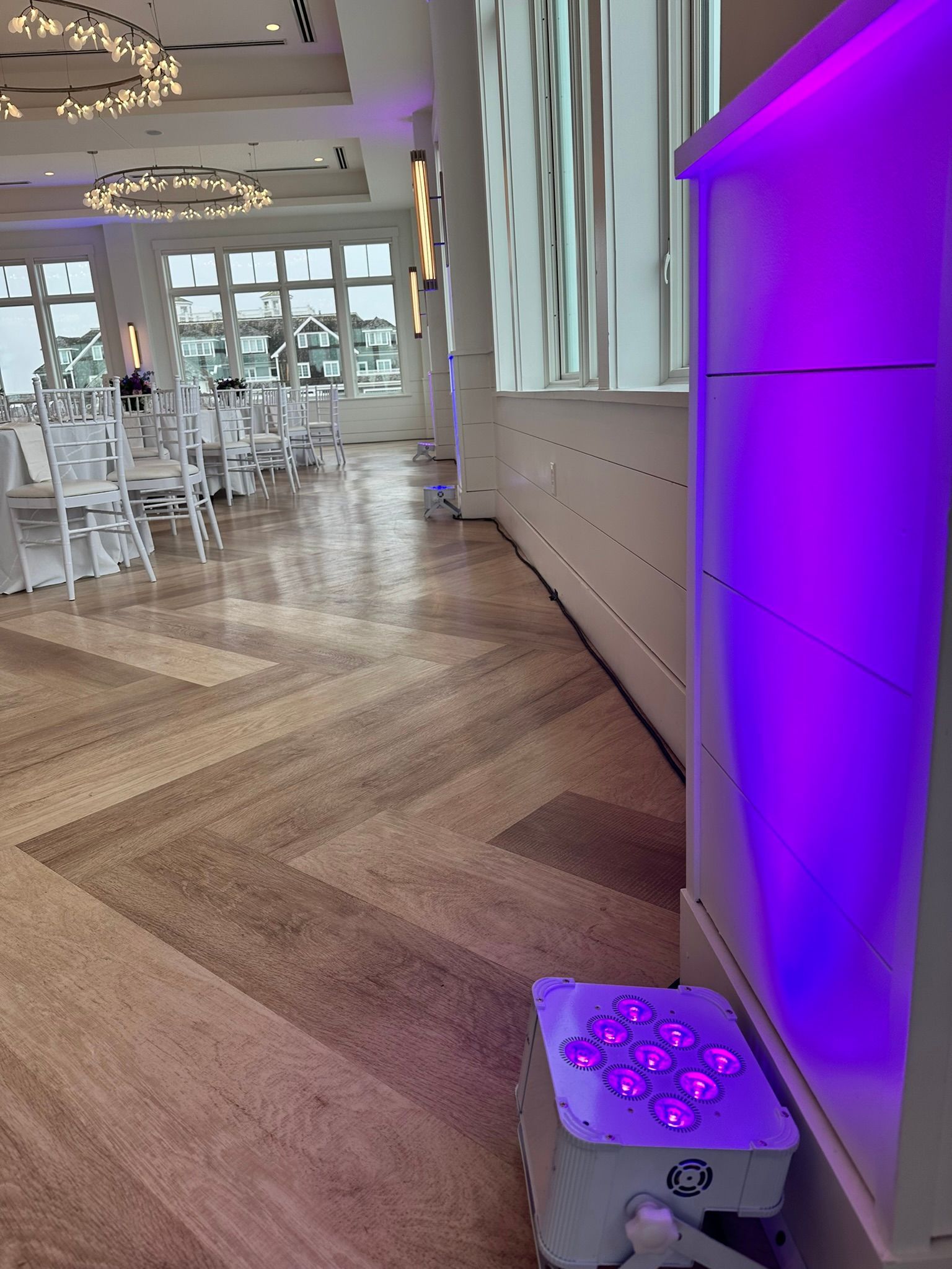 Interior of a venue with purple lighting illuminating a pillar. Tables and chairs are set up, wooden floor.
