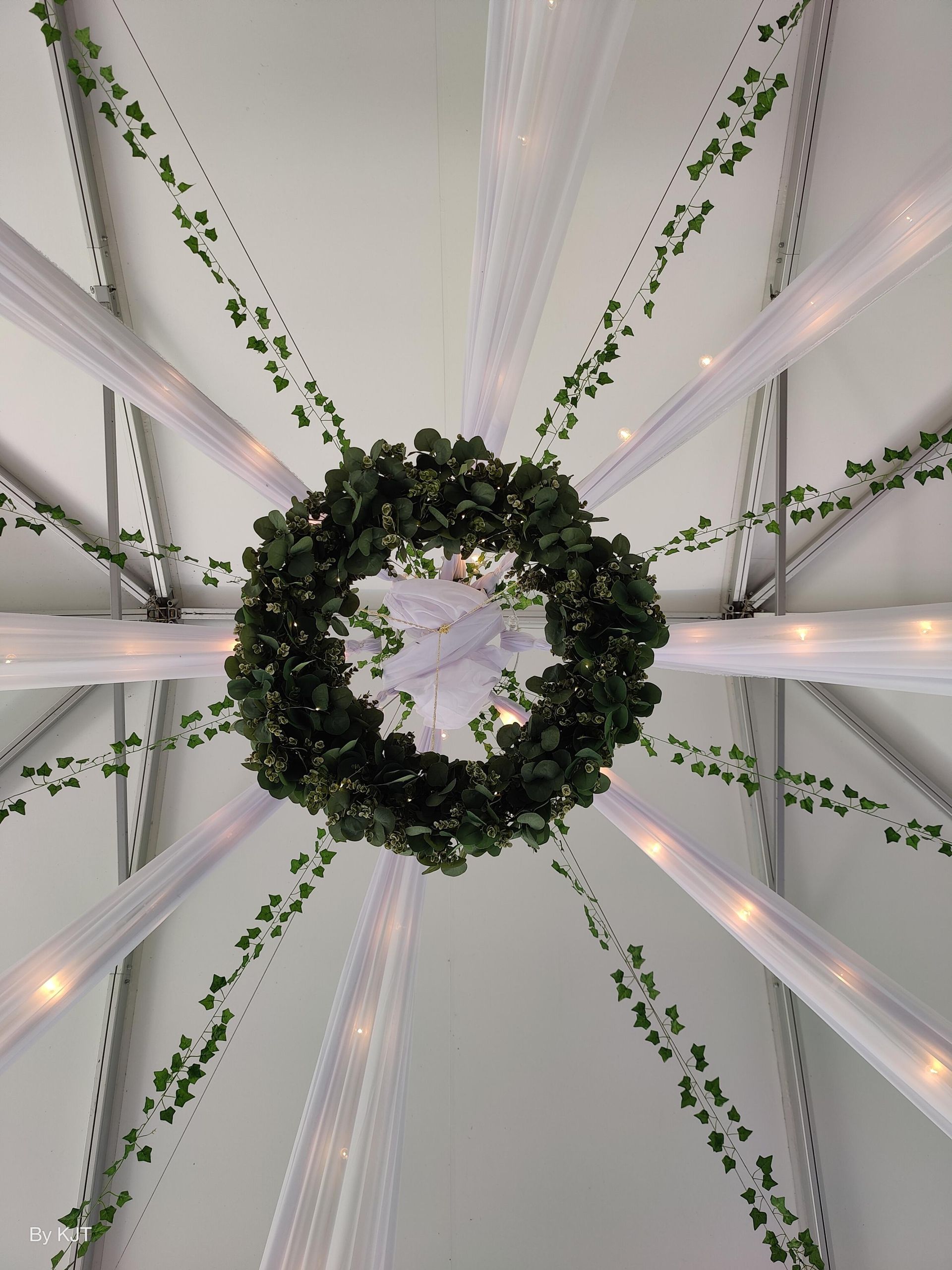 Ceiling decorated with white fabric, green vines, and a wreath. Strings of lights are also present.