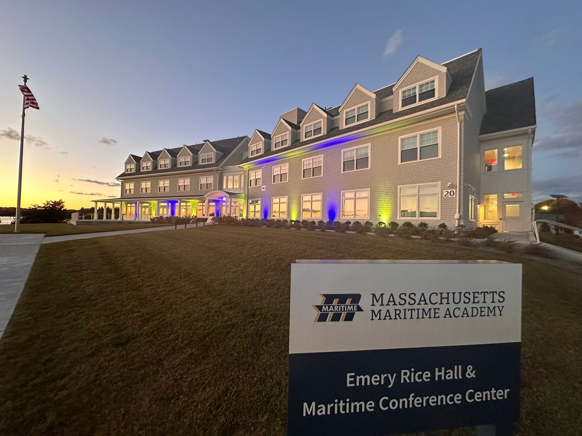 Massachusetts Maritime Academy building with sign at dusk, illuminated with colored lights.
