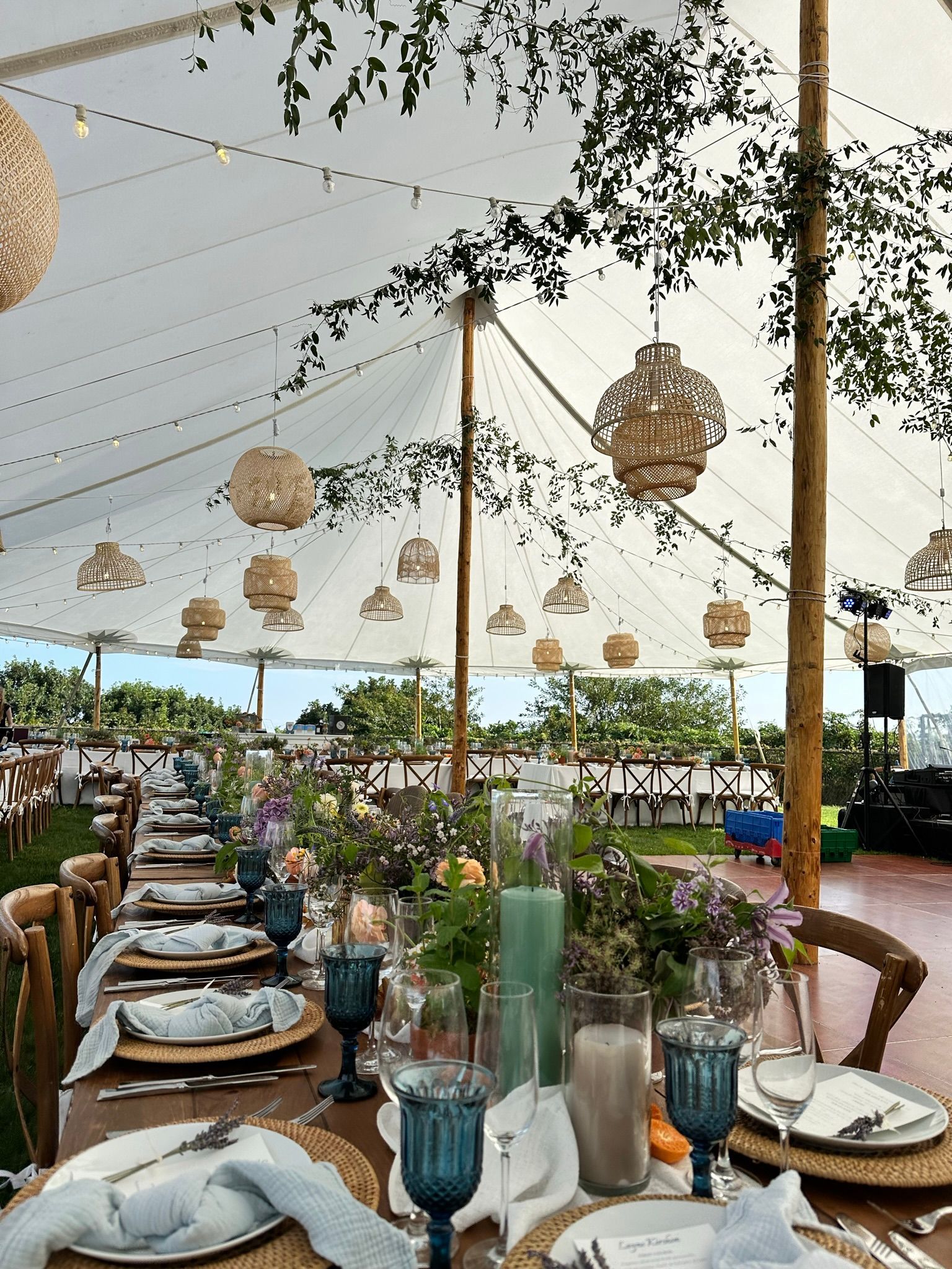 Long wedding table set under a tent with hanging lanterns and floral centerpieces.