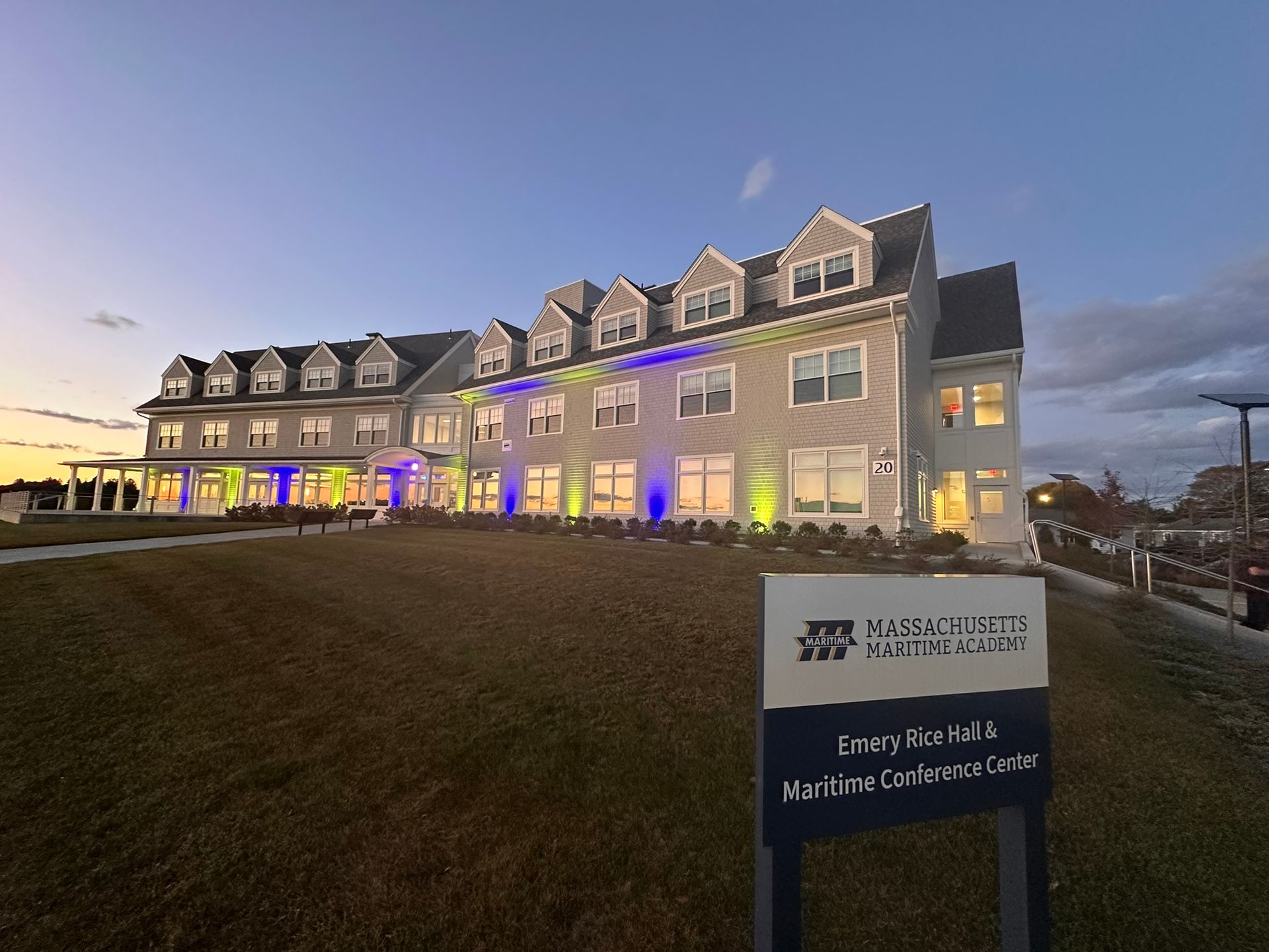 Building exterior with sign; illuminated with blue and green lights at dusk.