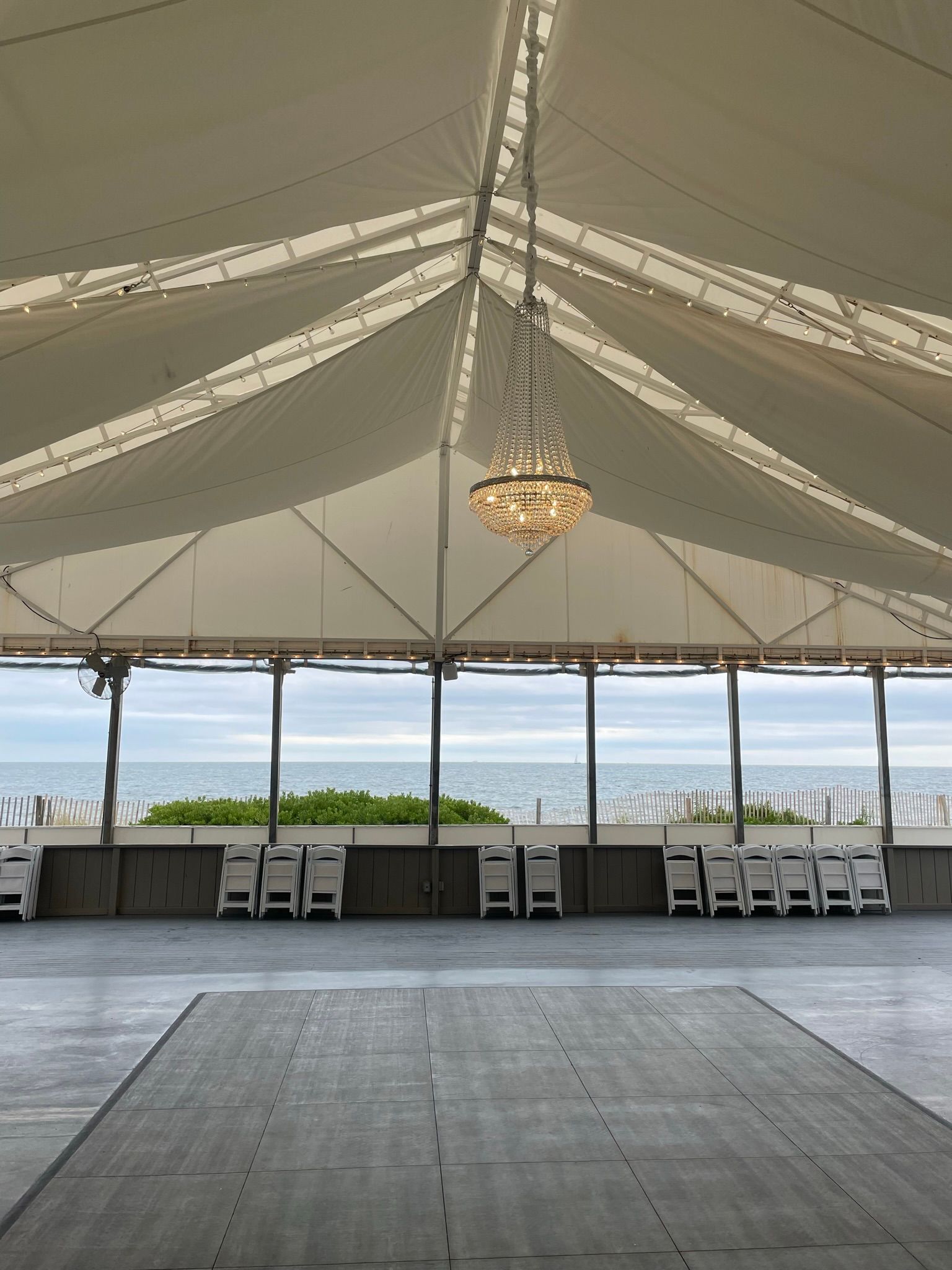 Inside a white tent with a chandelier, overlooking a beach and ocean.