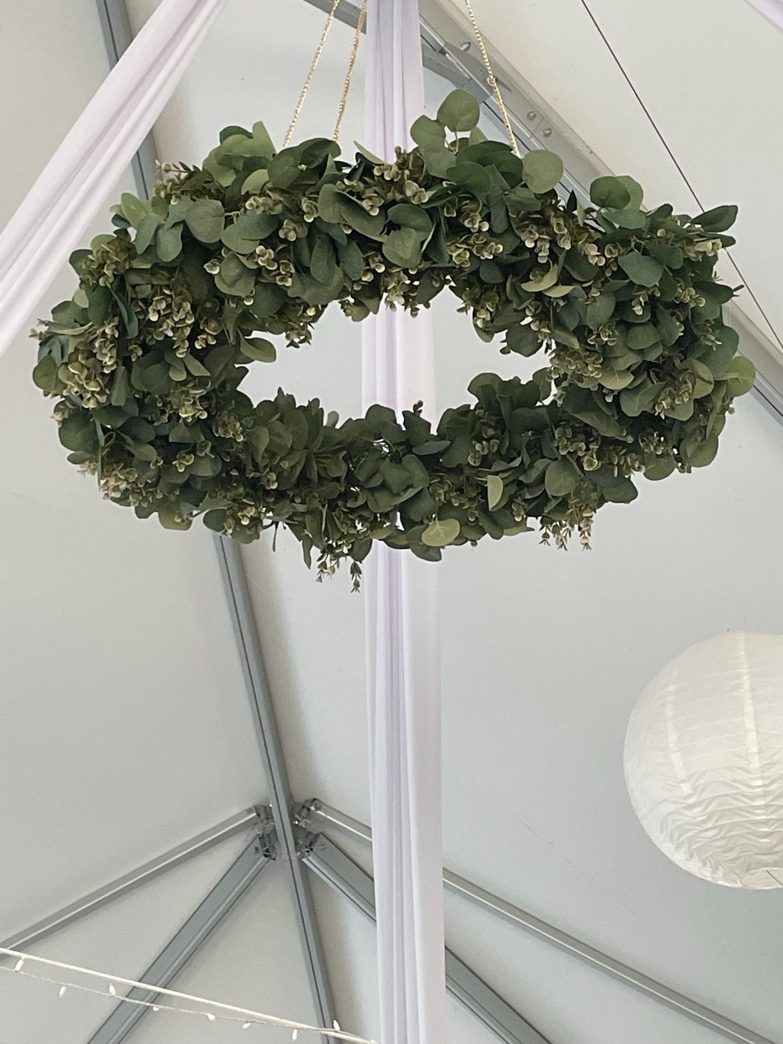 Green floral wreath hanging from a white tent ceiling.