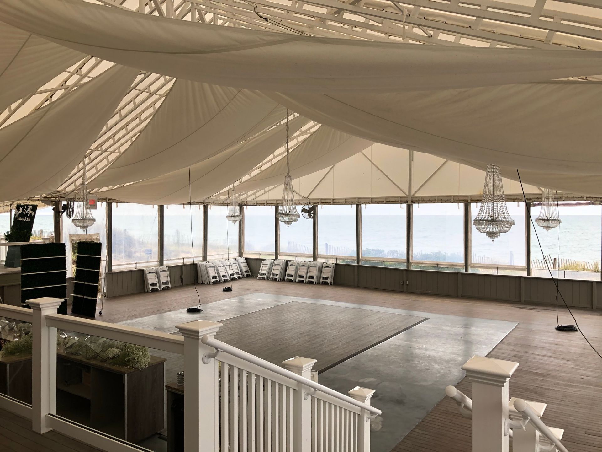 Interior of a large event tent with chandeliers, dance floor, and a view through windows.