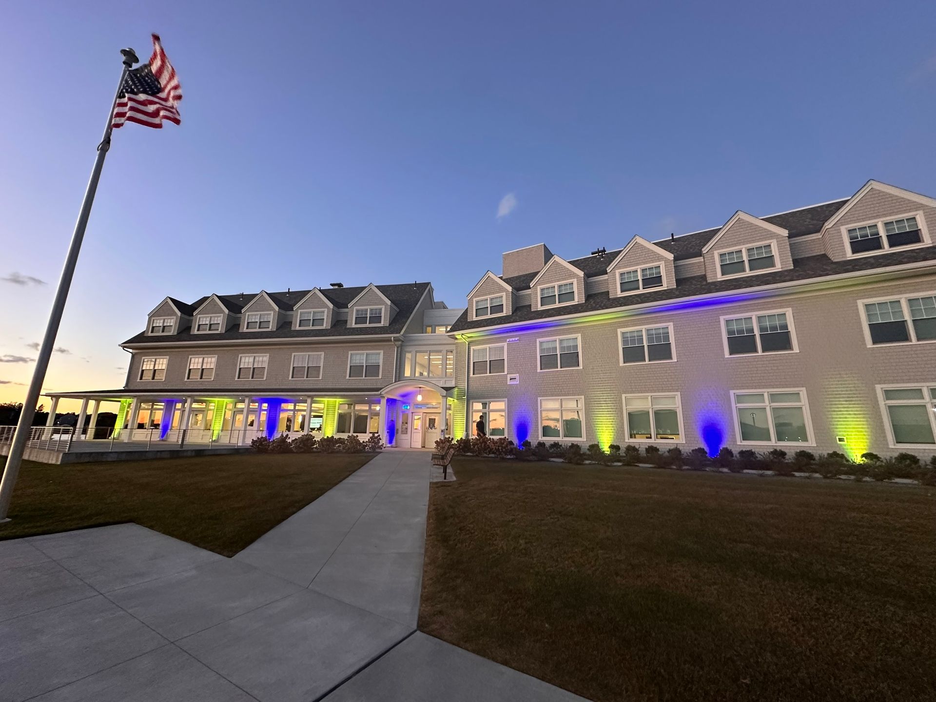 Building with American flag at dusk, illuminated with blue and green lights.